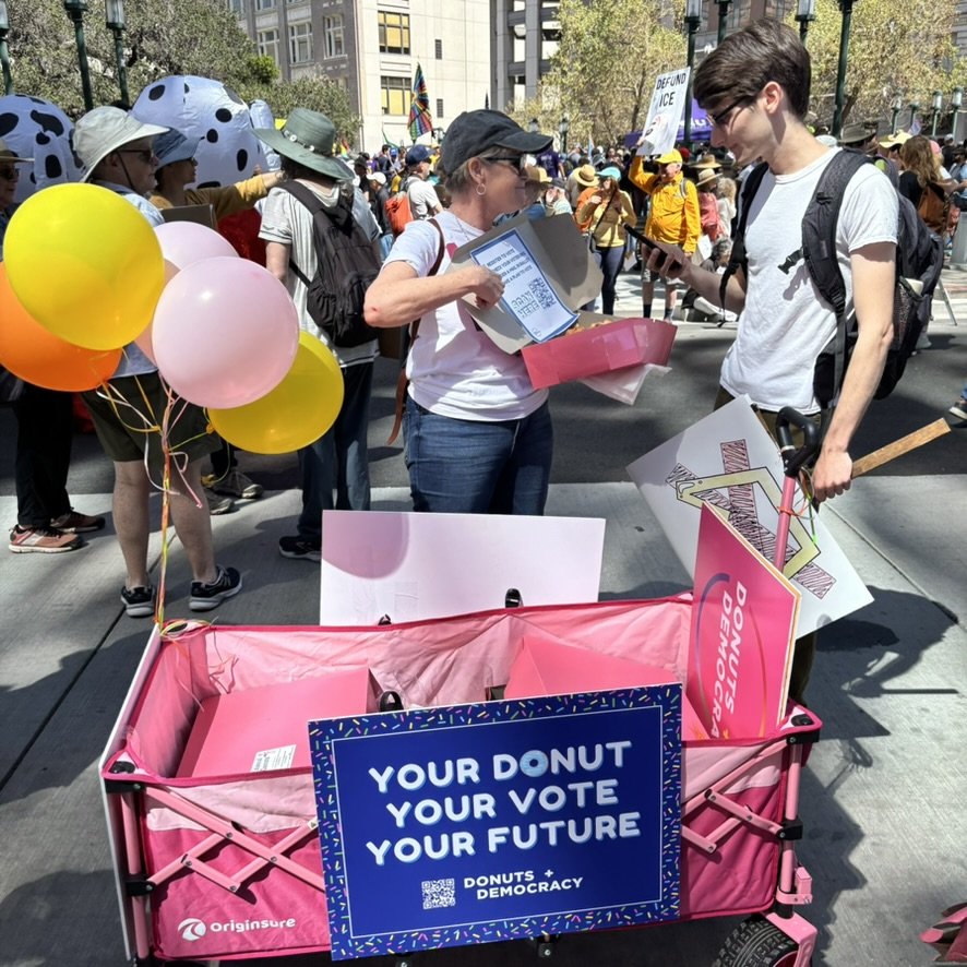 Two people discussing voting in front of a donut wagon
