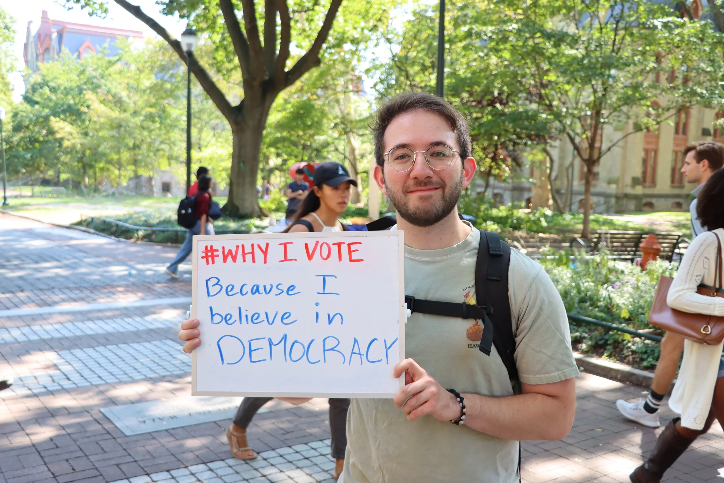 A person holding a sign that says "#Why I vote: Because I believe in democracy"