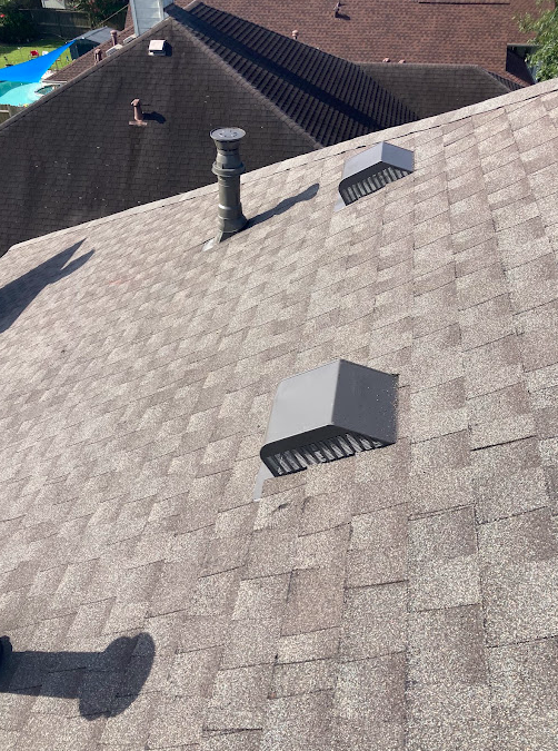 View of a residential roof with vents and a chimney, showing shingles and neighboring rooftops.