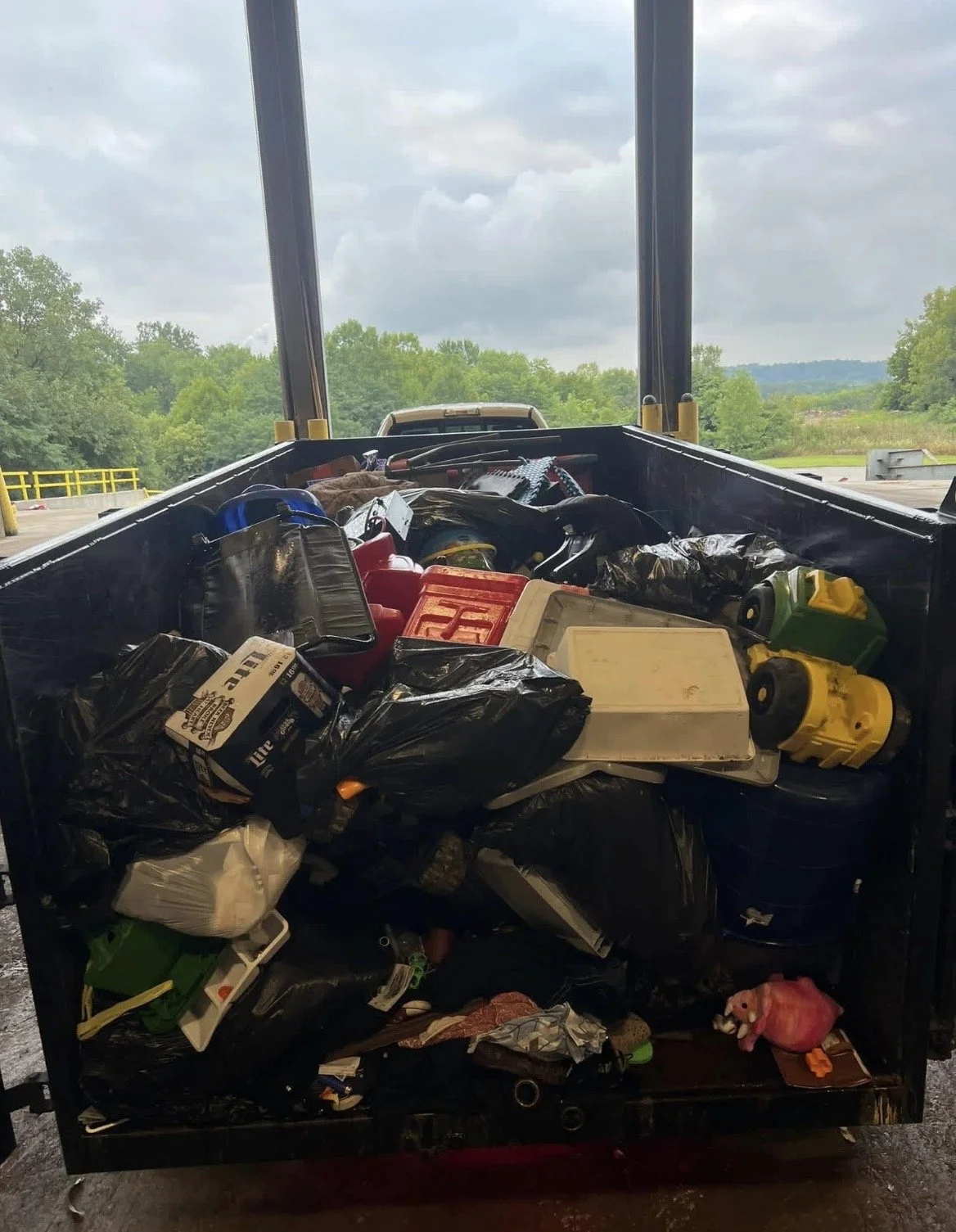 A trailer filled with various tools, supplies, and containers parked outdoors on a cloudy day, with trees and a landscape in the background.