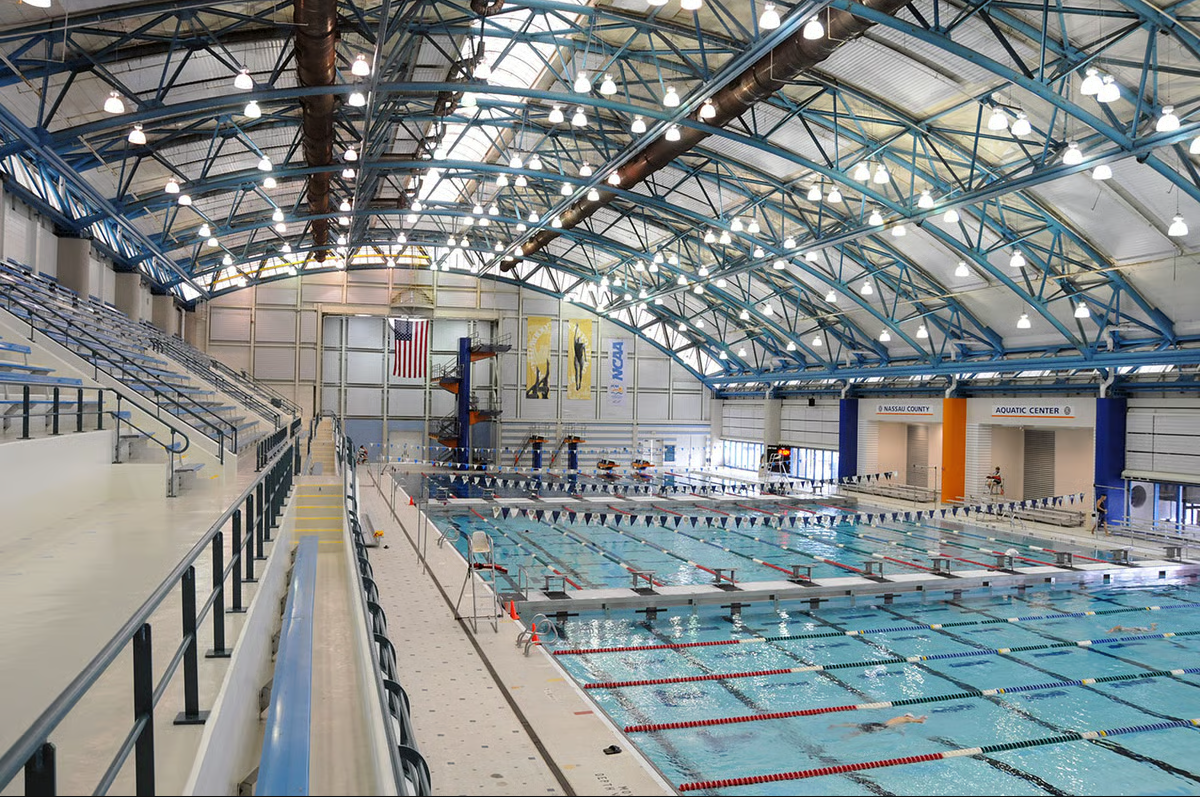 Indoor swimming pool with lanes, water slides, and seating area under a high arched ceiling with lights.