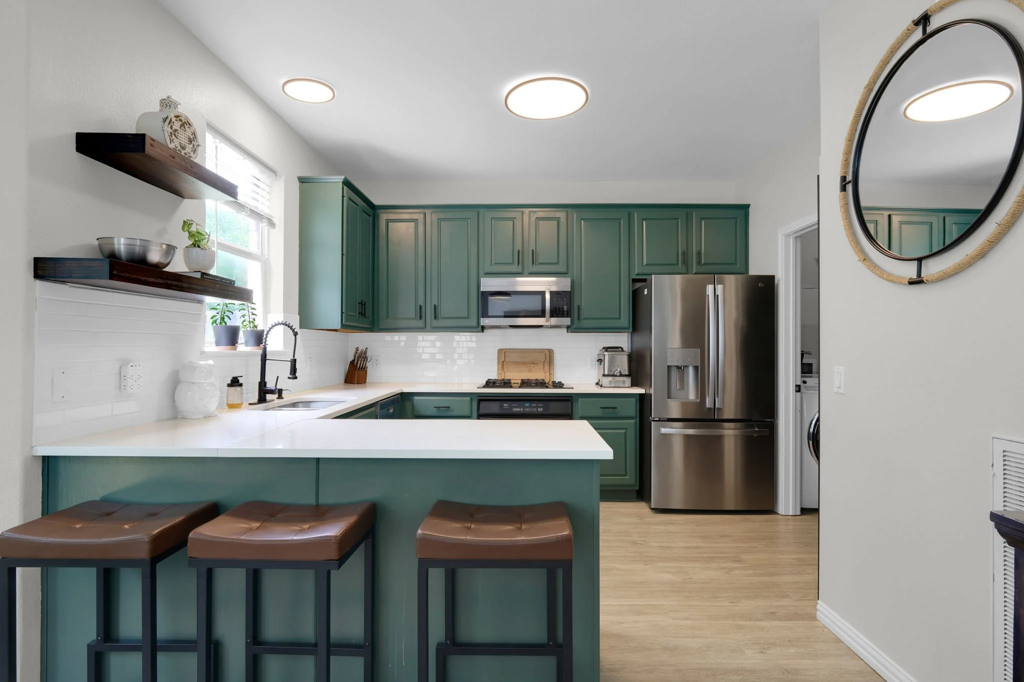Modern kitchen with green cabinets, stainless steel refrigerator, microwave, and white countertop with barstools