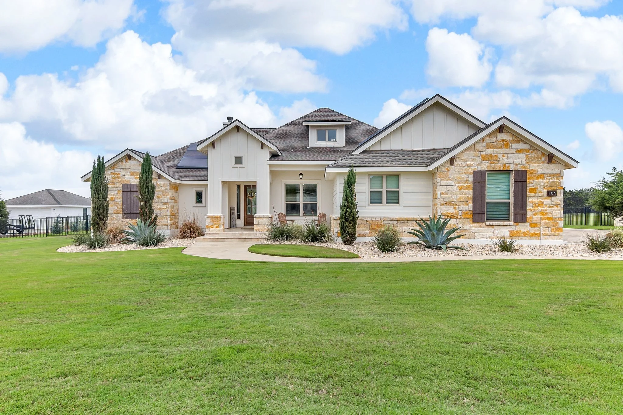 Front view of a two-story house with stone and siding exterior, surrounded by a well-maintained lawn and landscaped yard, under a partly cloudy sky.