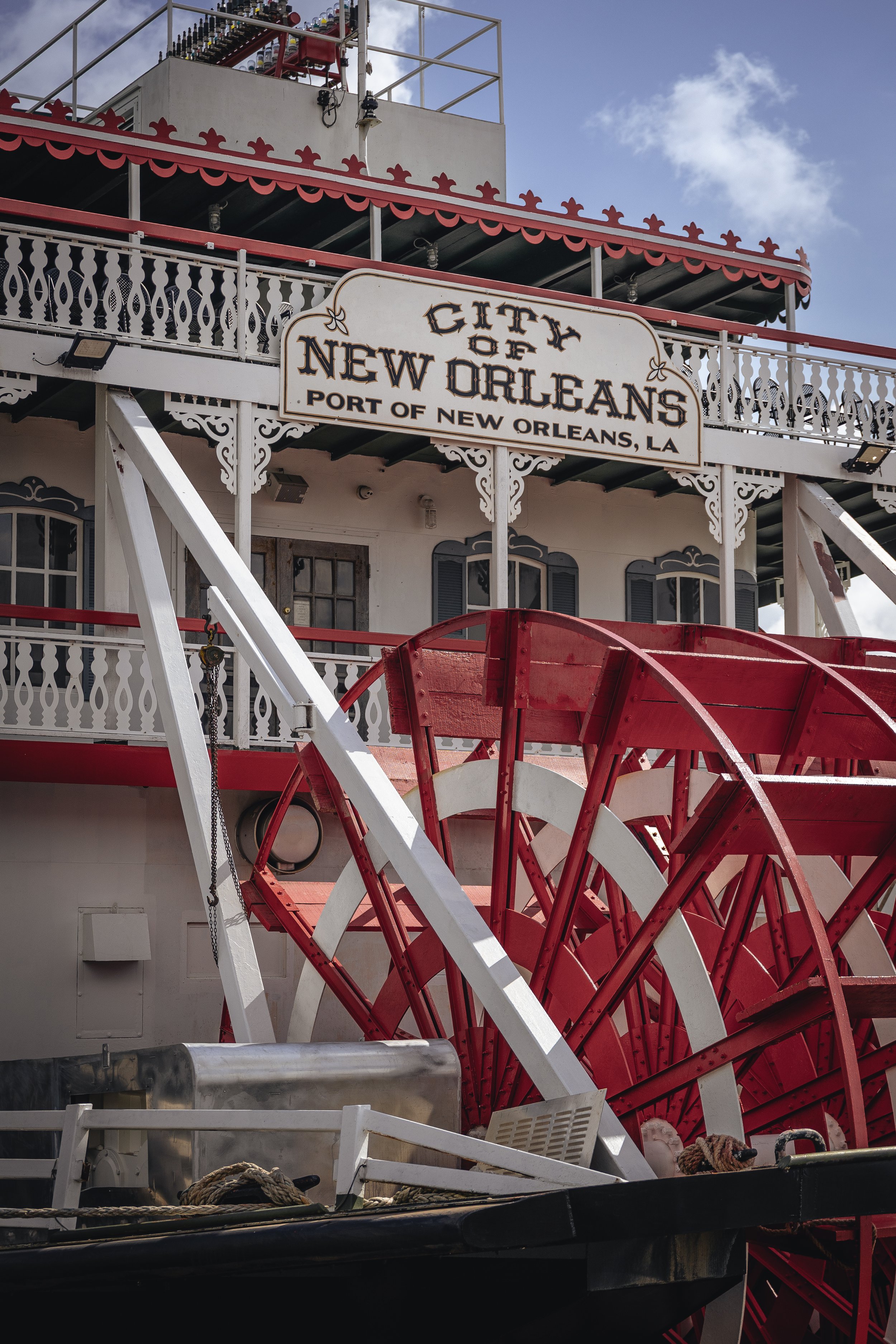 A red and white Ferris wheel on a boat, with a sign reading, 'City of New Orleans, Port of New Orleans, LA,' and a building with decorative white railings and windows in the background.