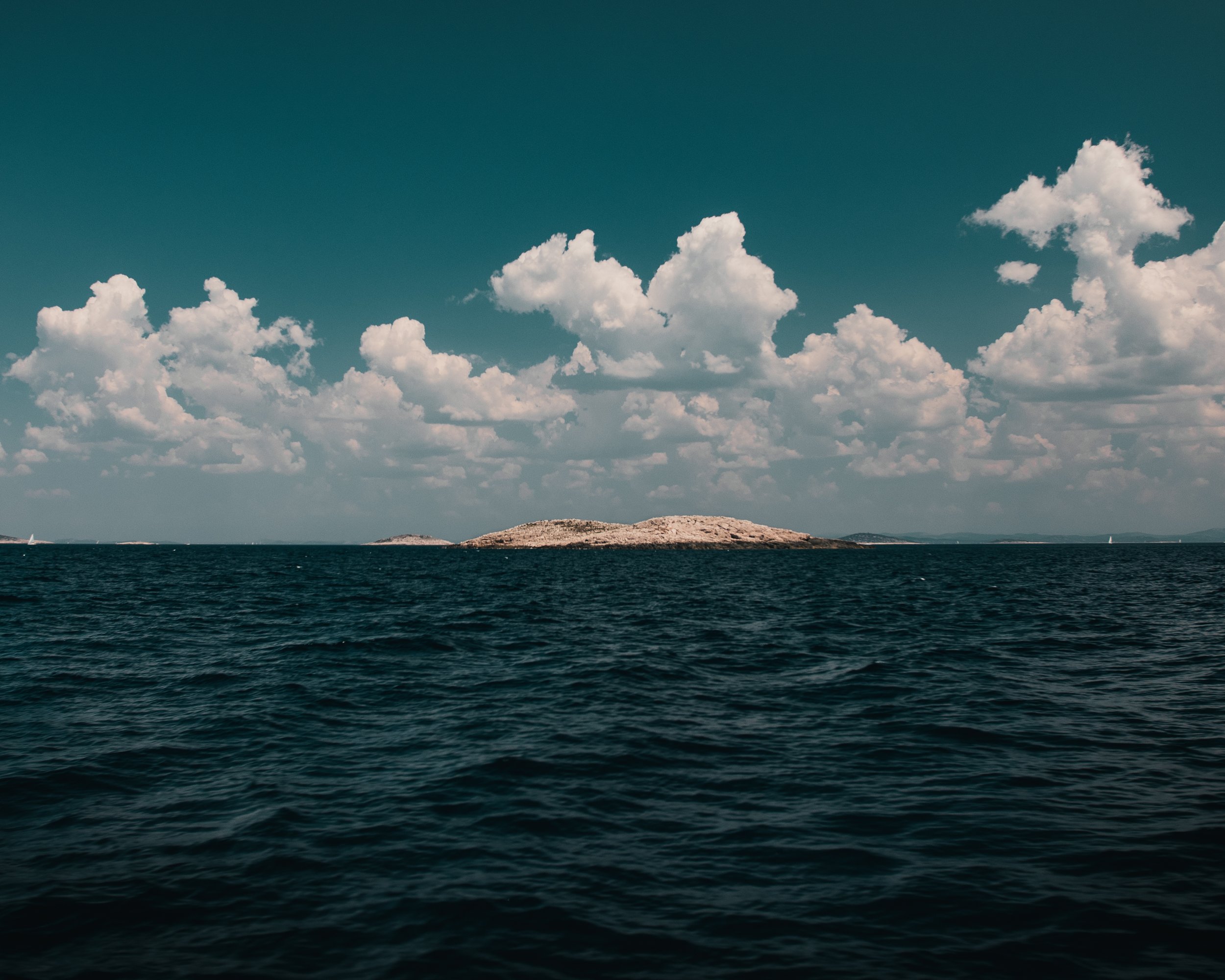 A body of water with small waves, a rocky island in the distance, and a clear sky with scattered clouds.