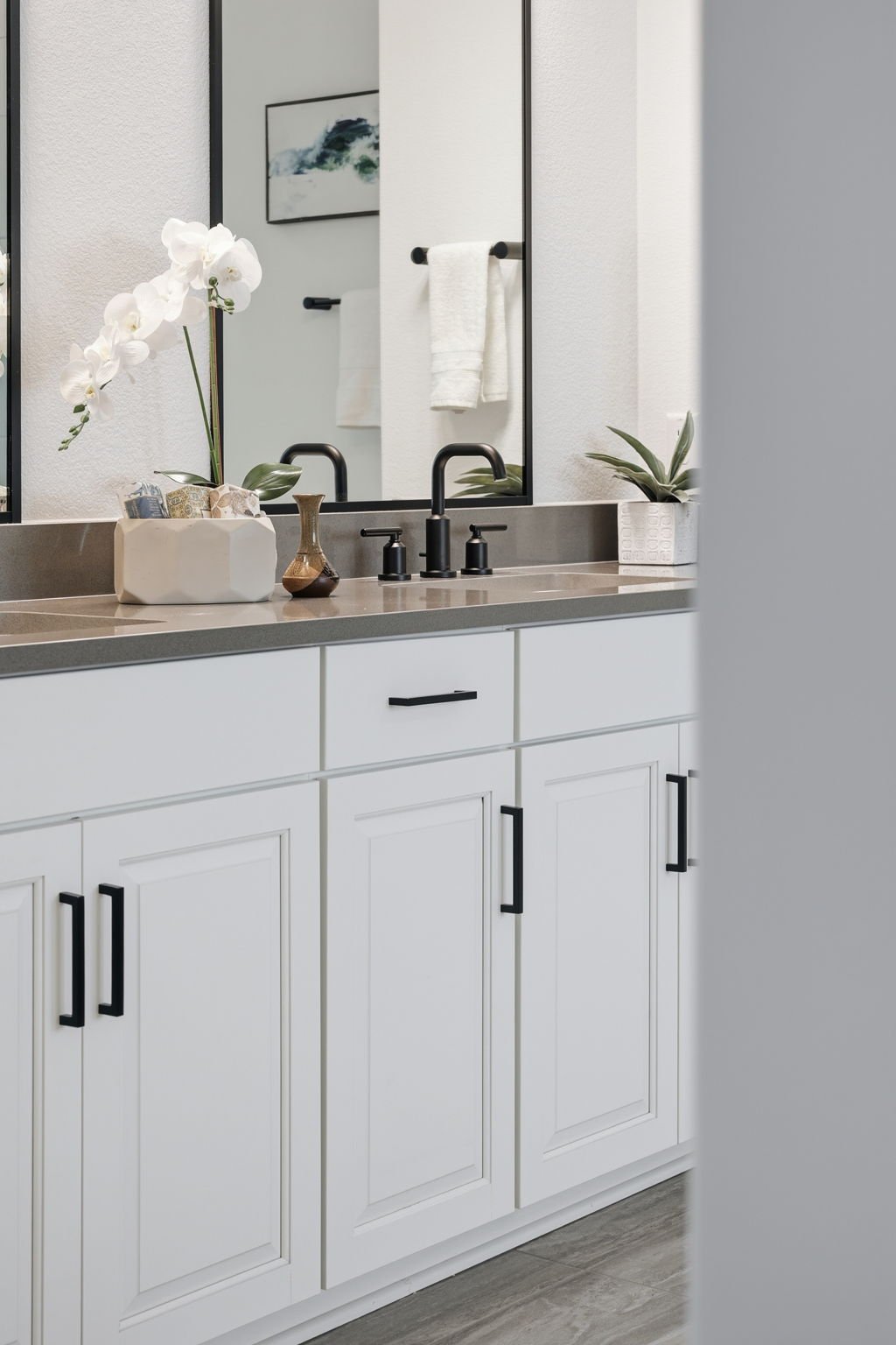 Bathroom vanity with white cabinets, a gray countertop, a large mirror, and decorative plants.