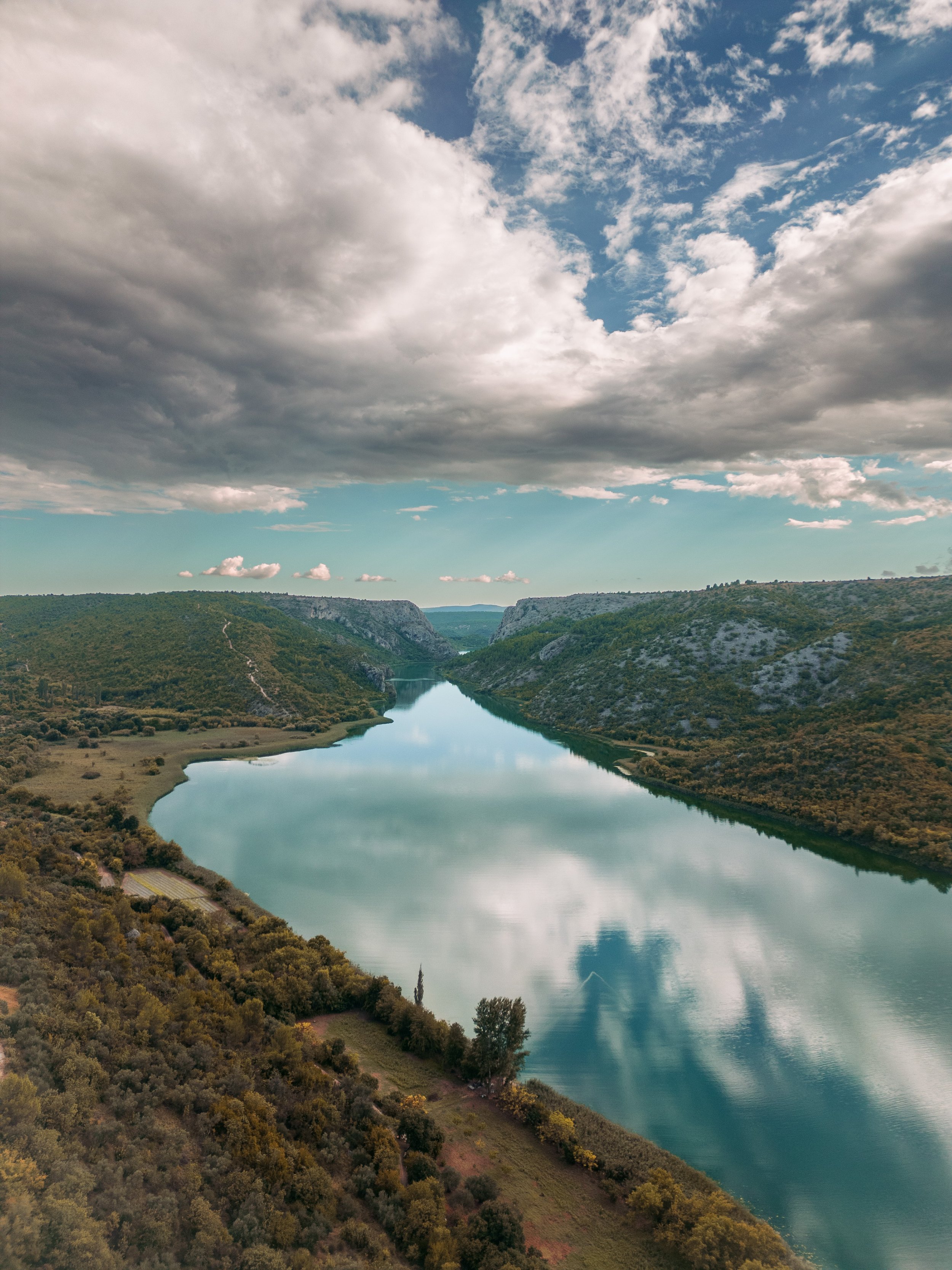A winding river flows between green hills under a partly cloudy sky.
