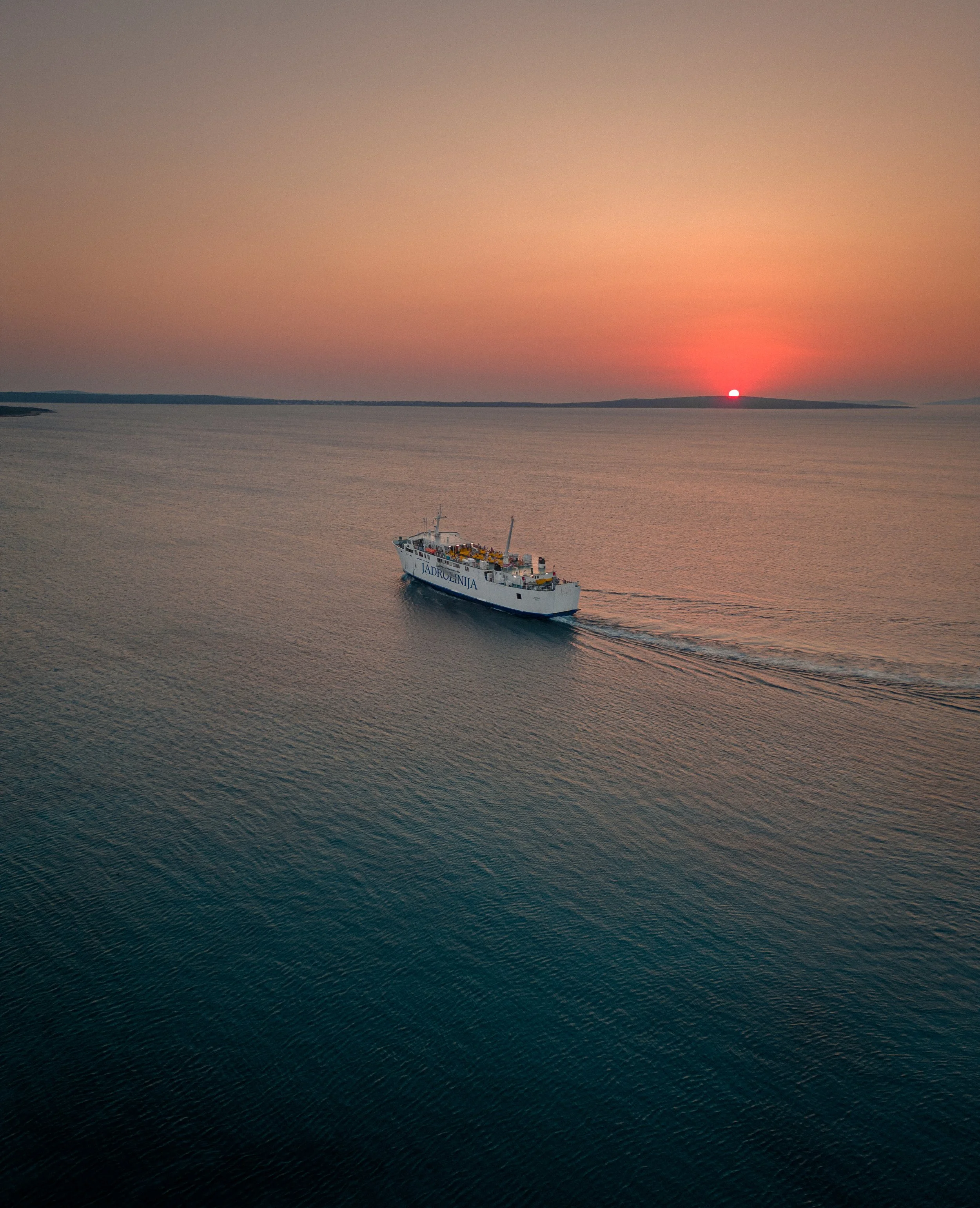 A cruise ship sailing on calm water during sunset with a distant landmass in the background.