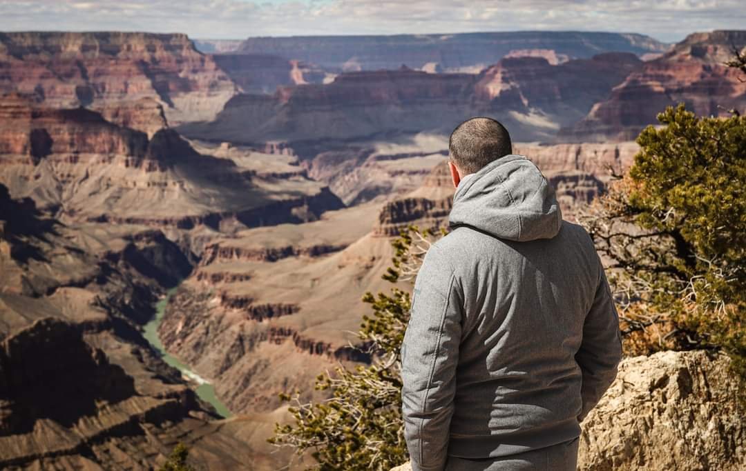 Man wearing a gray hoodie looking out over the Grand Canyon.