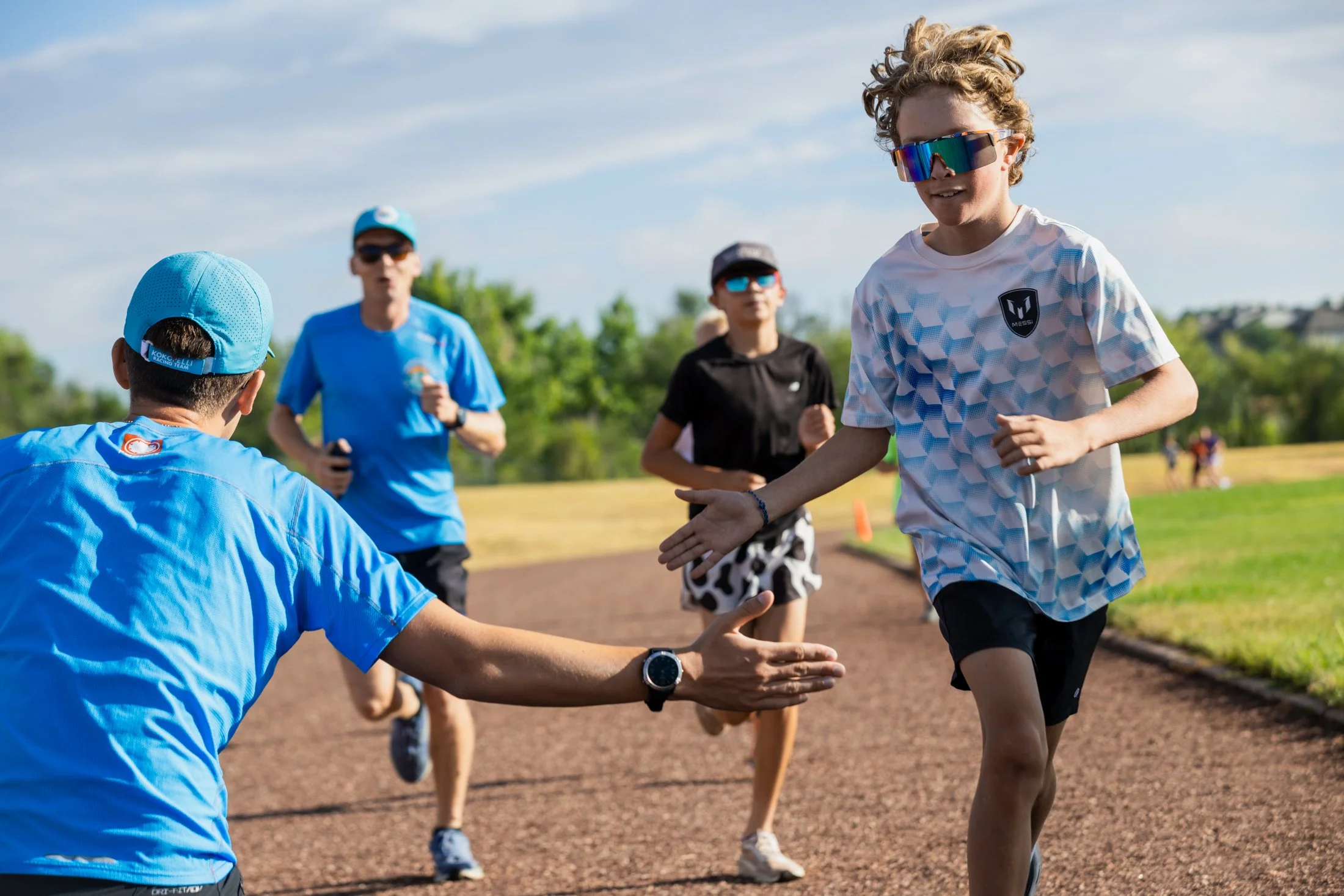 Group of people outdoors on a track field, with some rushing and others greeting with handshakes or high-fives, under blue sky.