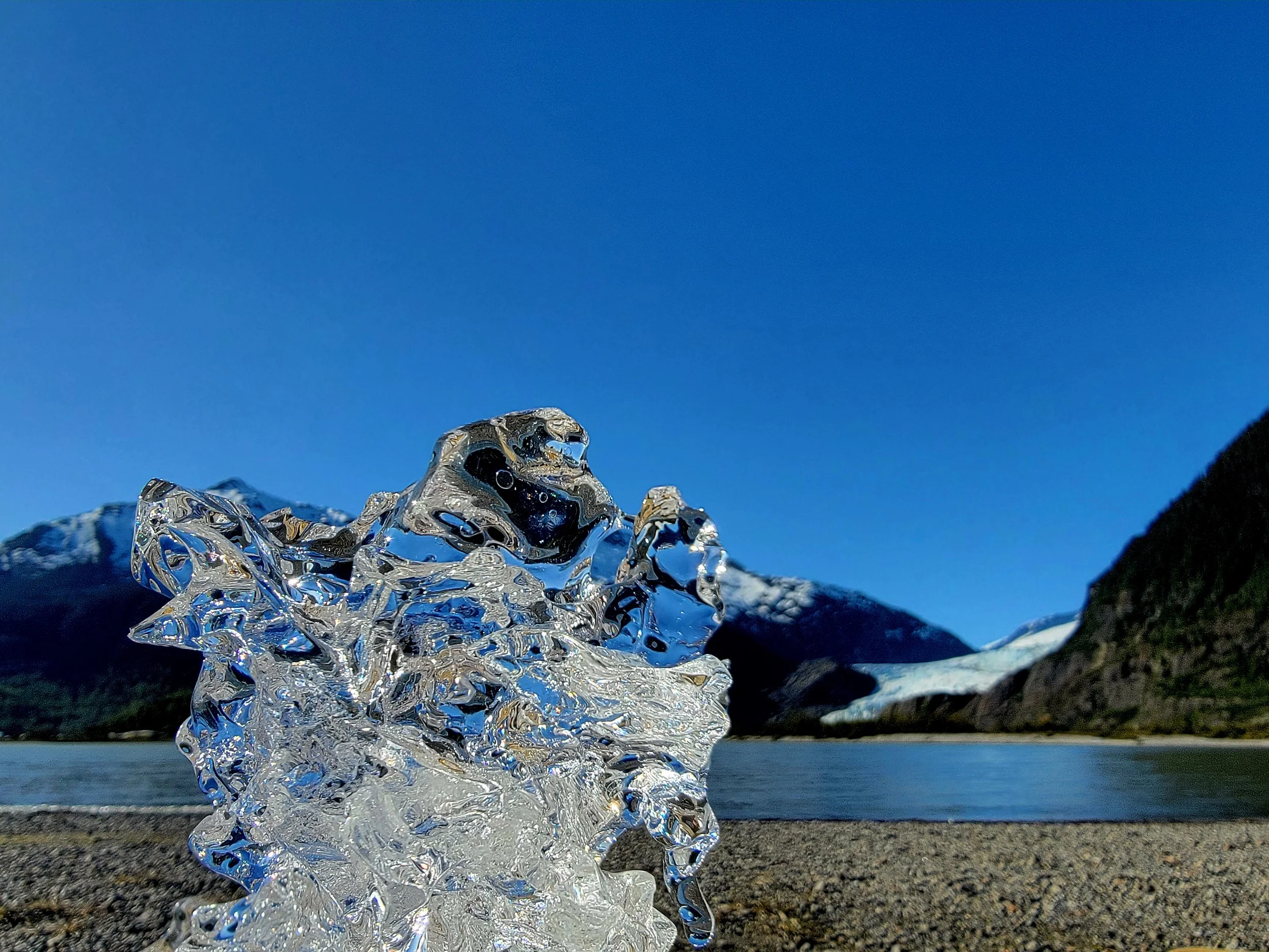 Close-up of a water splash or ice crystal formation with mountains in the background under a clear blue sky.