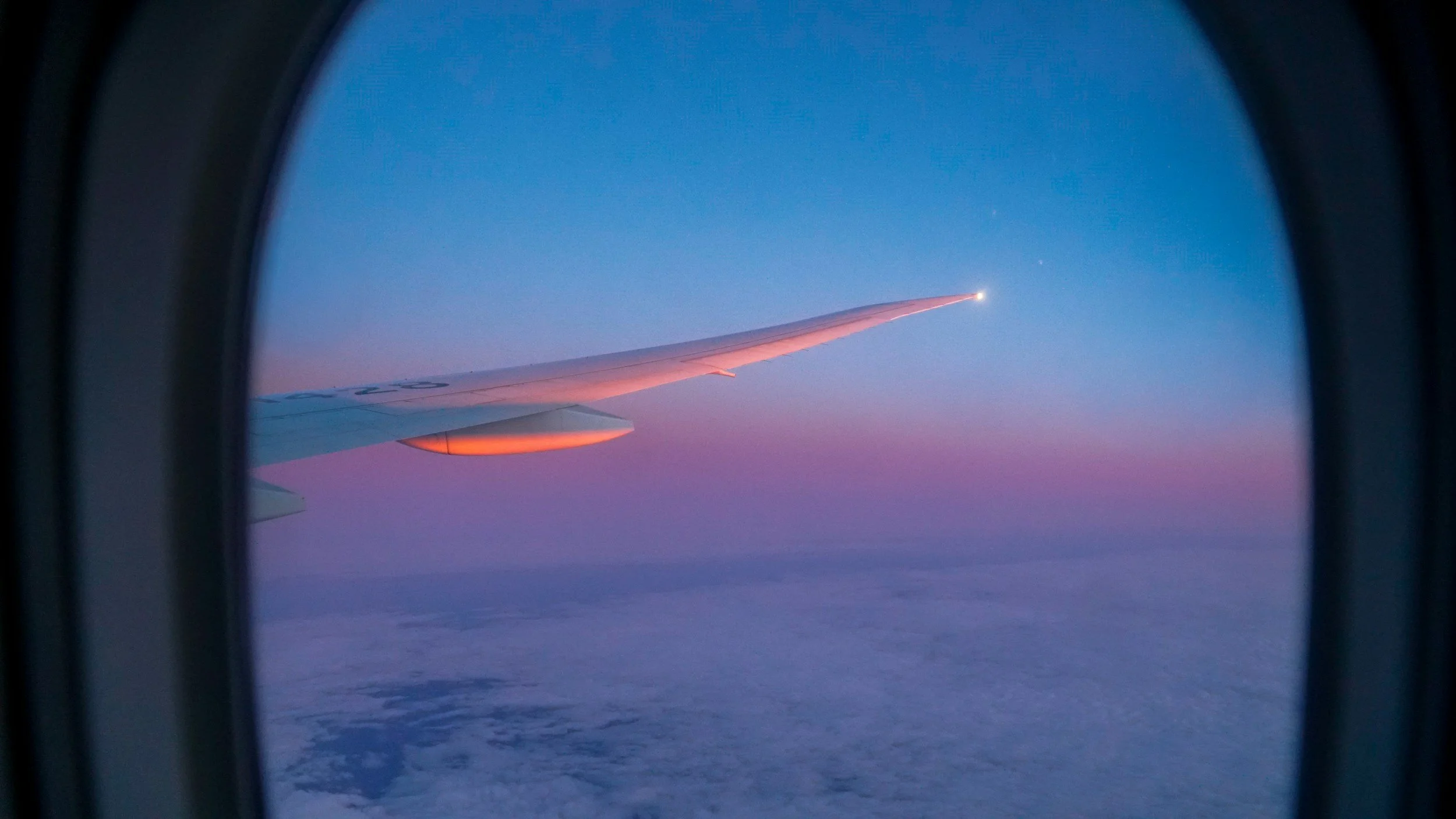 View of an airplane wing from an airplane window during dusk or dawn, with a pink and purple sky.