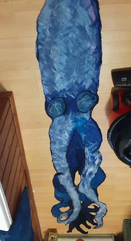A blue and gray abstract painting of an octopus on a wooden floor.
