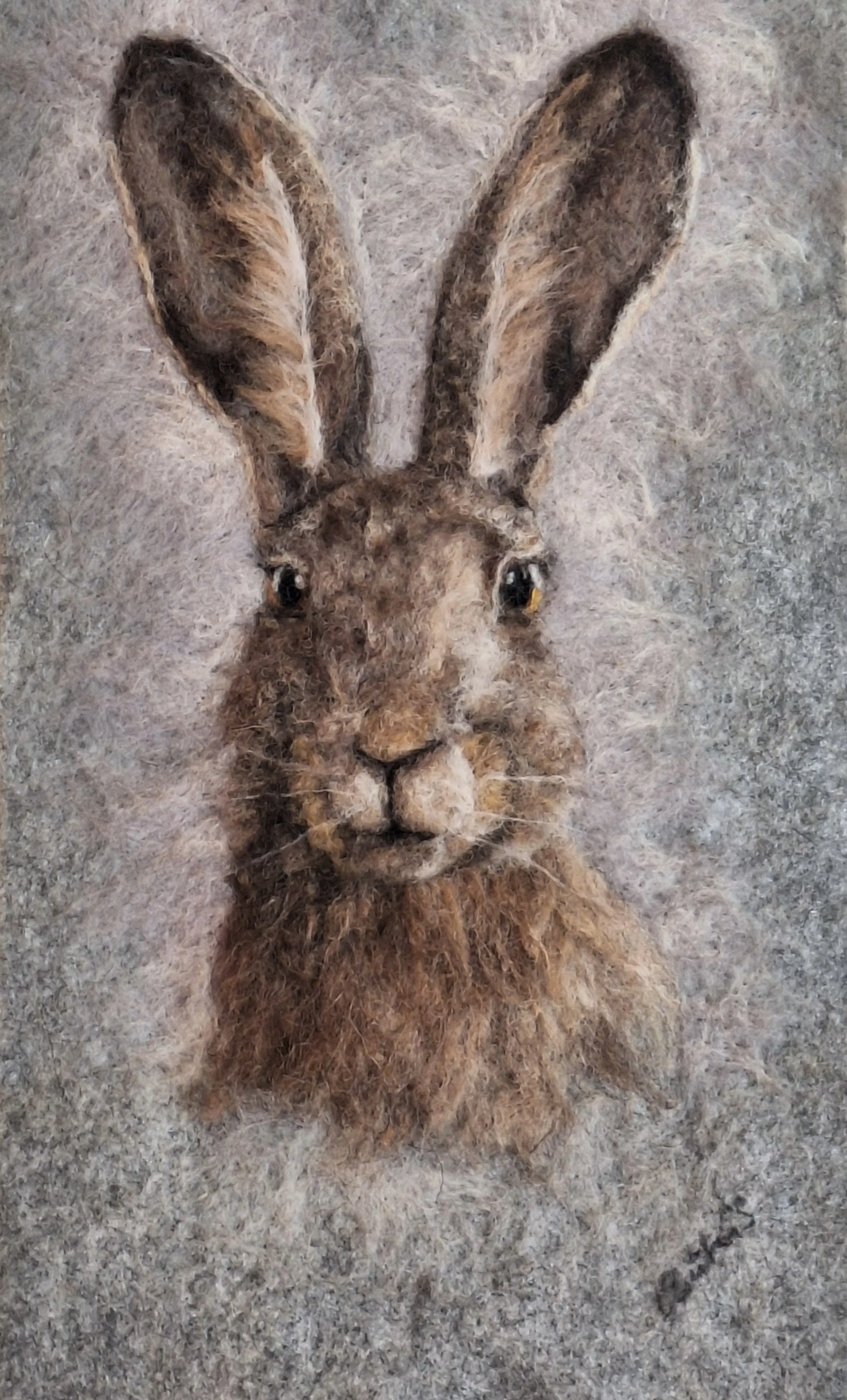 Felted wool artwork of a rabbit's face with large ears, detailed eyes, nose, and fur texture on a neutral background.