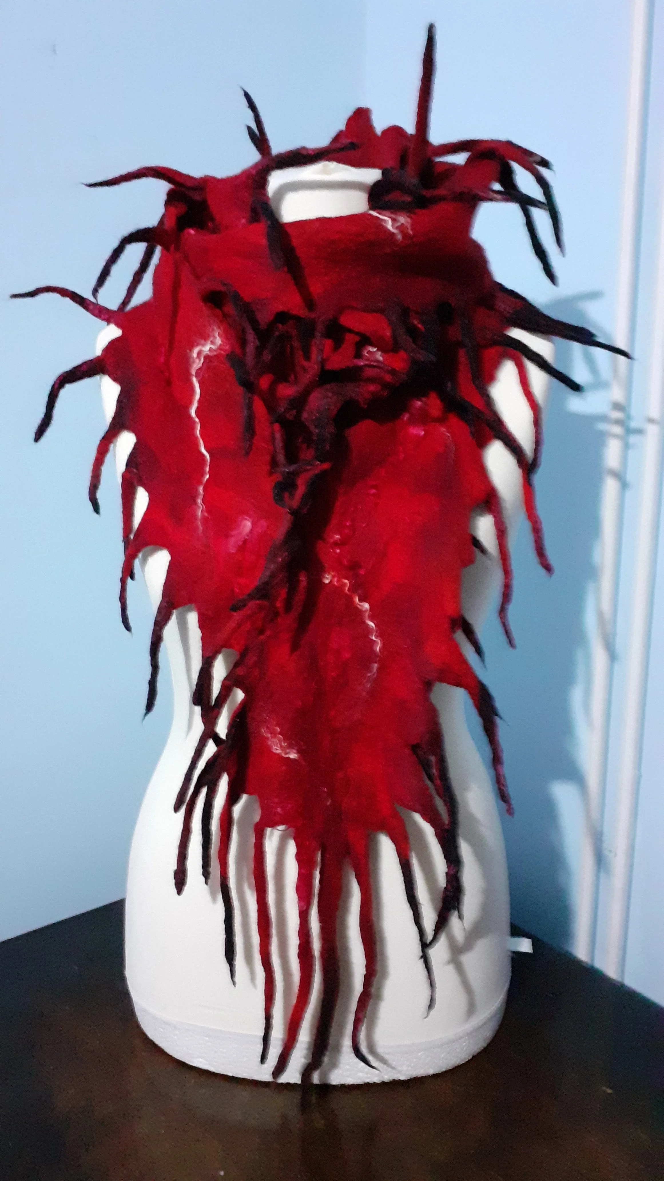 A mannequin head display with a red and black wig, styled with long, twisted, and spiky strands, on a white styrofoam mannequin head.
