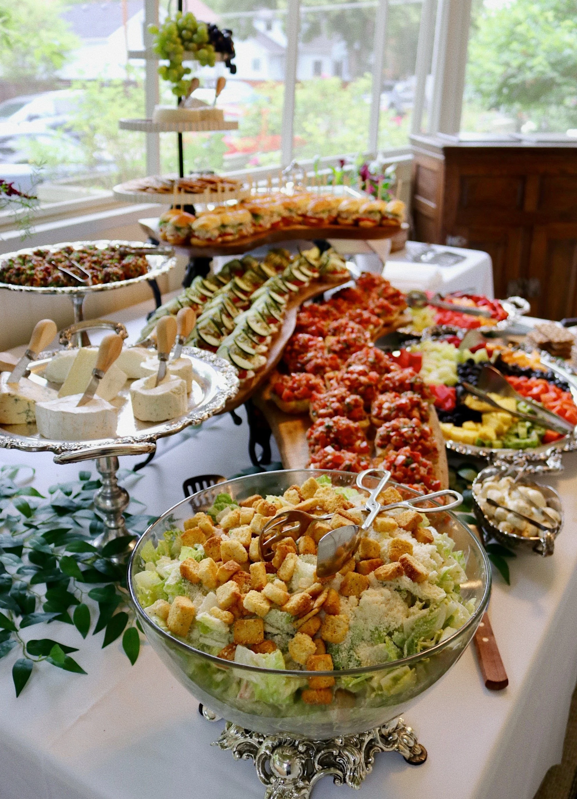 Large bowl of Caesar salad with assorted cheeses and bruschetta and more appetizers prepared by Silver Platter Catering