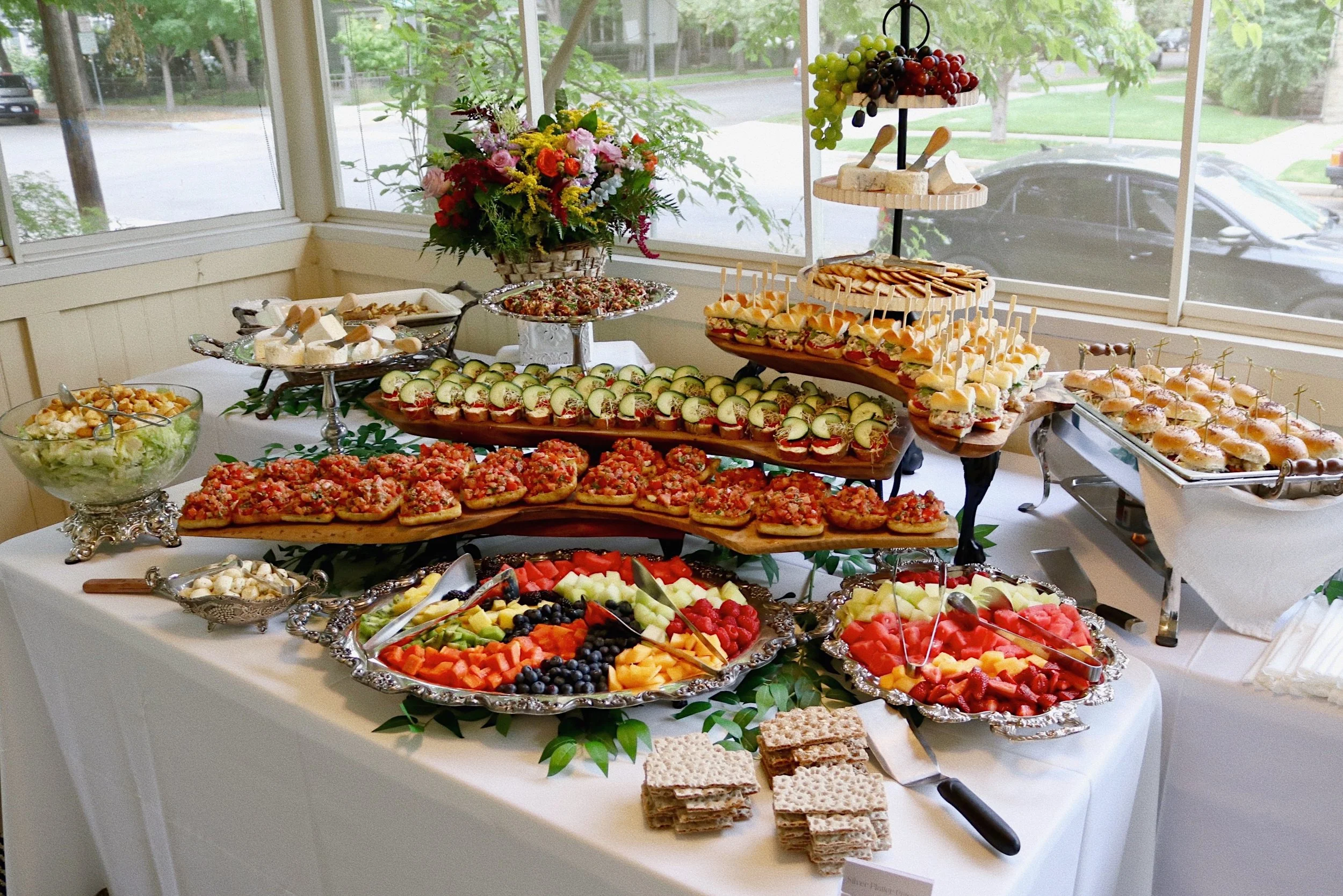 Assortment of bruschetta, cucumber sandwiches, Buffalo Chicken Salad sliders, assorted fruit, and Caesar salad prepared by Silver Platter Catering
