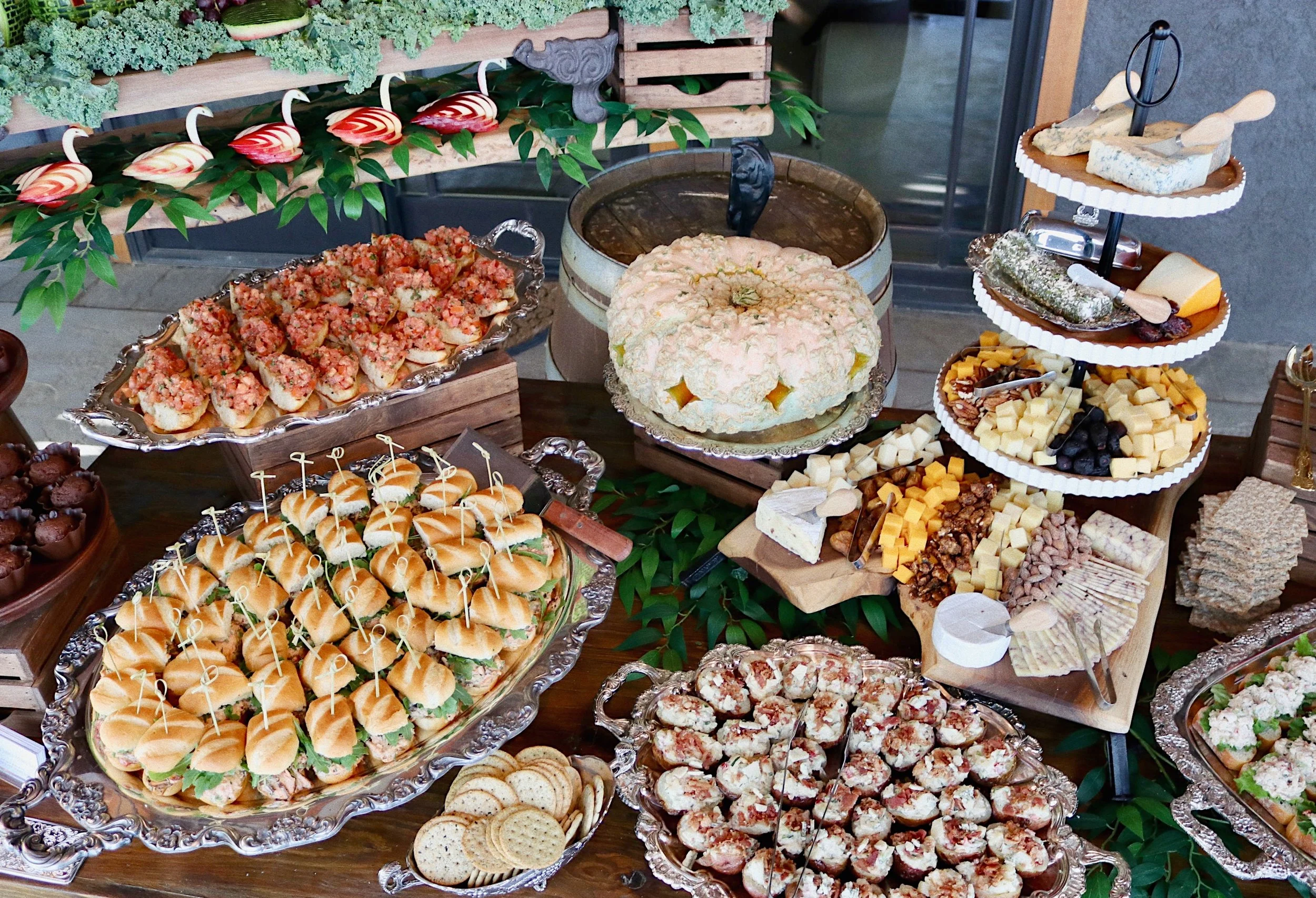 Appetizer table featuring Buffalo Chicken Salad sliders, mini stuffed baked potatoes, mini bruschetta, carved apple ducks, and an assortment of cheeses and crackers, prepared by Silver Platter Catering