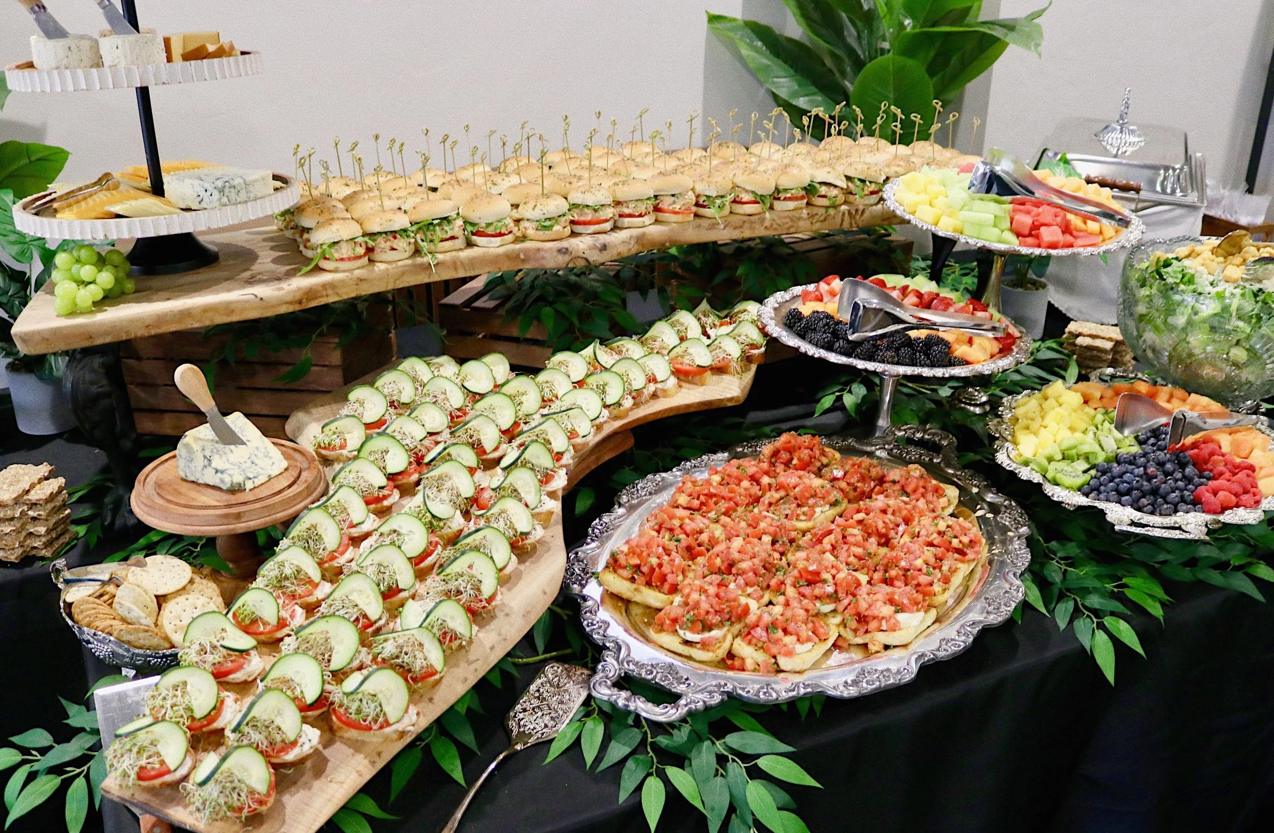 Appetizer table featuring smoked chicken salad sandwiches, cucumber sandwiches, assorted fruits, Caesar salad, and bruschetta, prepared by Silver Platter Catering