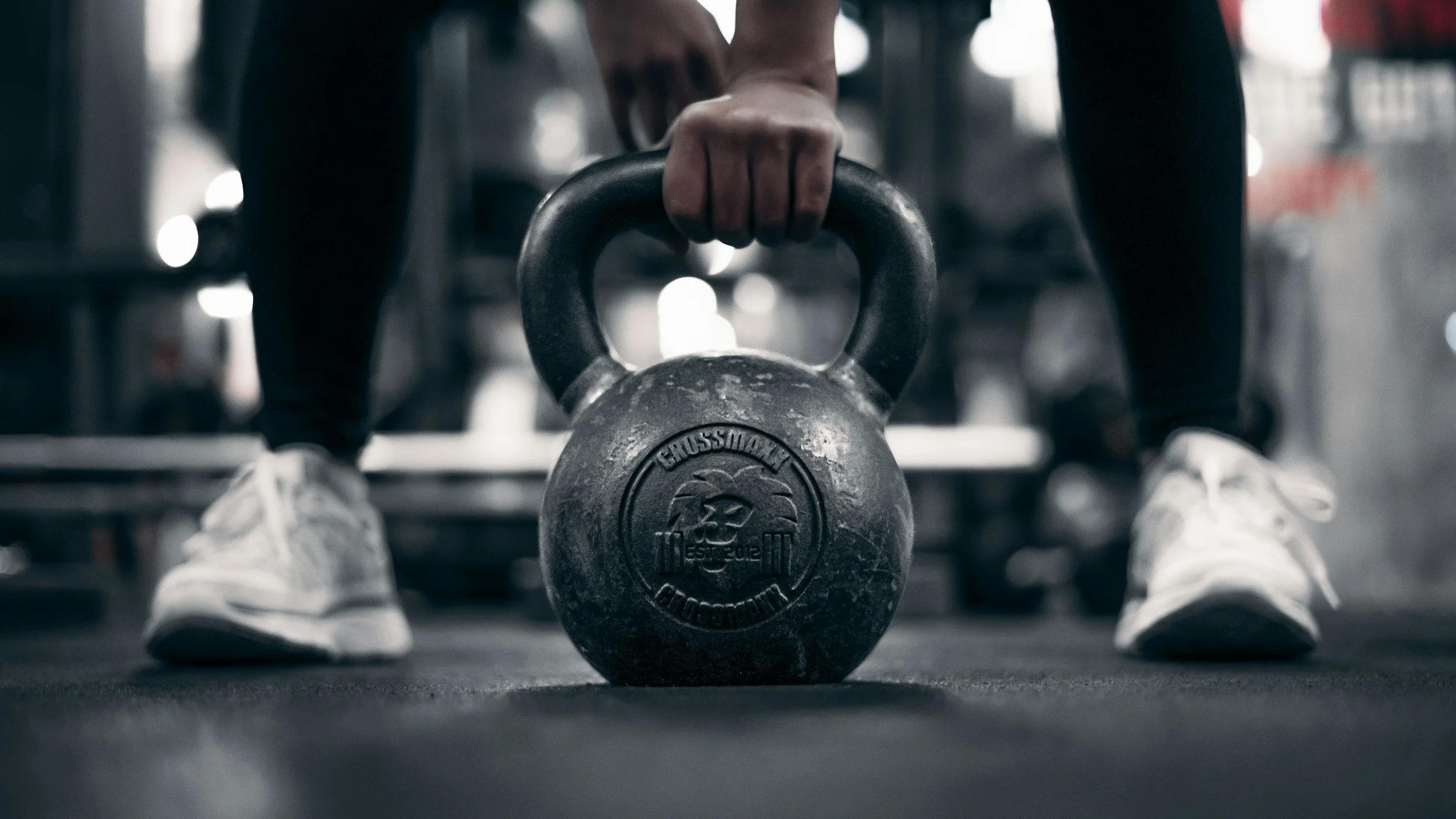 Close-up of a person holding a kettlebell during a workout, with gym equipment and blurred background.
