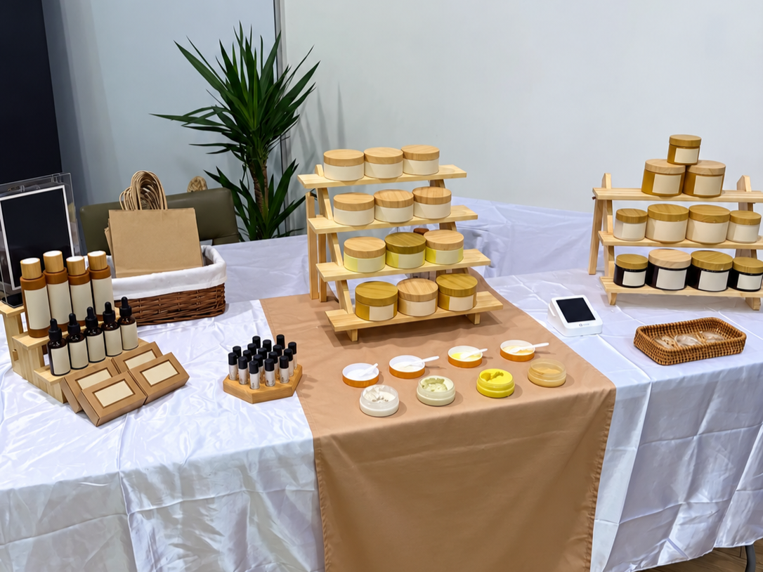 Display of skincare products including bottles, jars, and tubs on wooden shelves and tables at an exhibition or store.