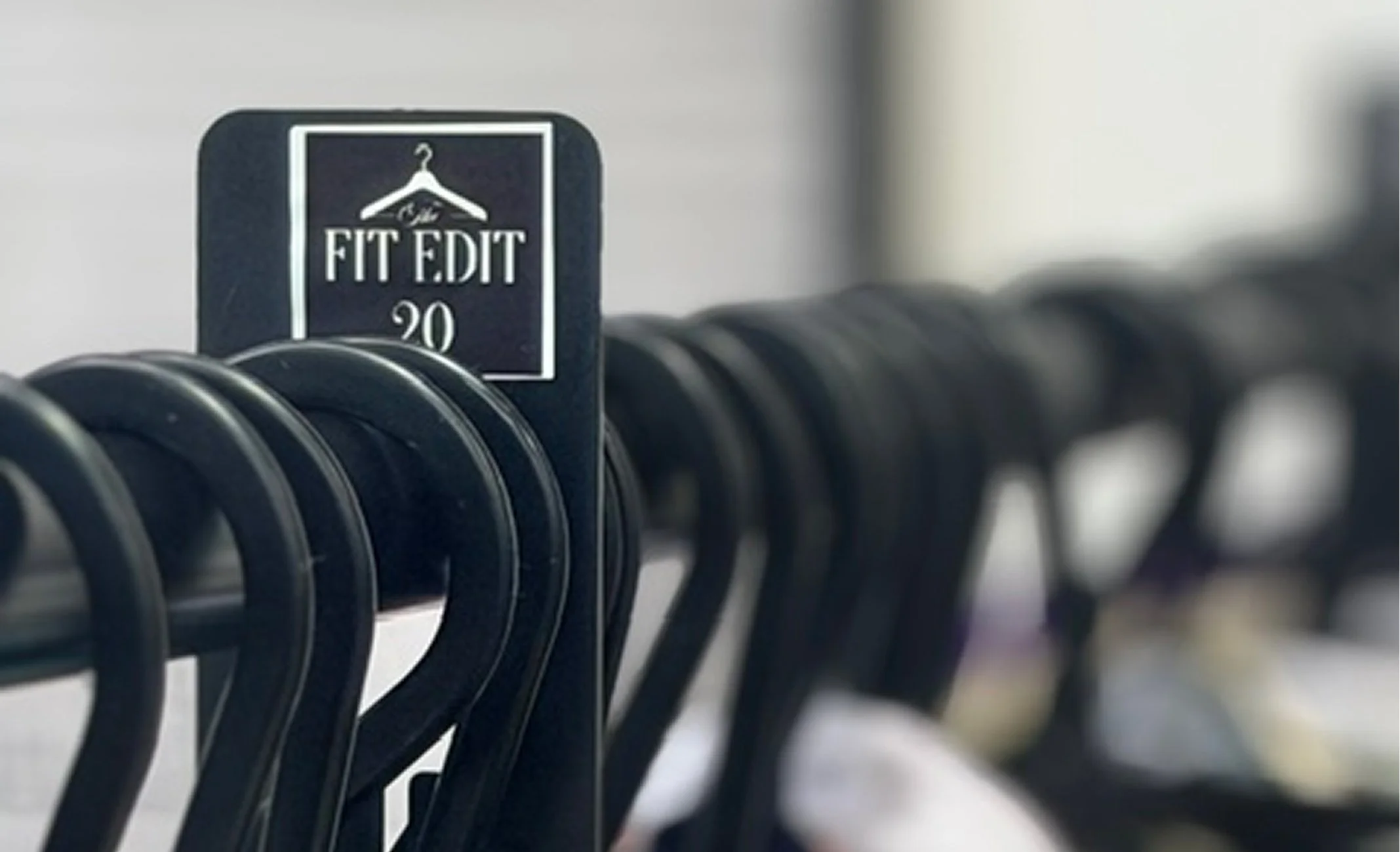 A clothing rack with black hangers displaying a black sign that reads "Fit & Edit 20."