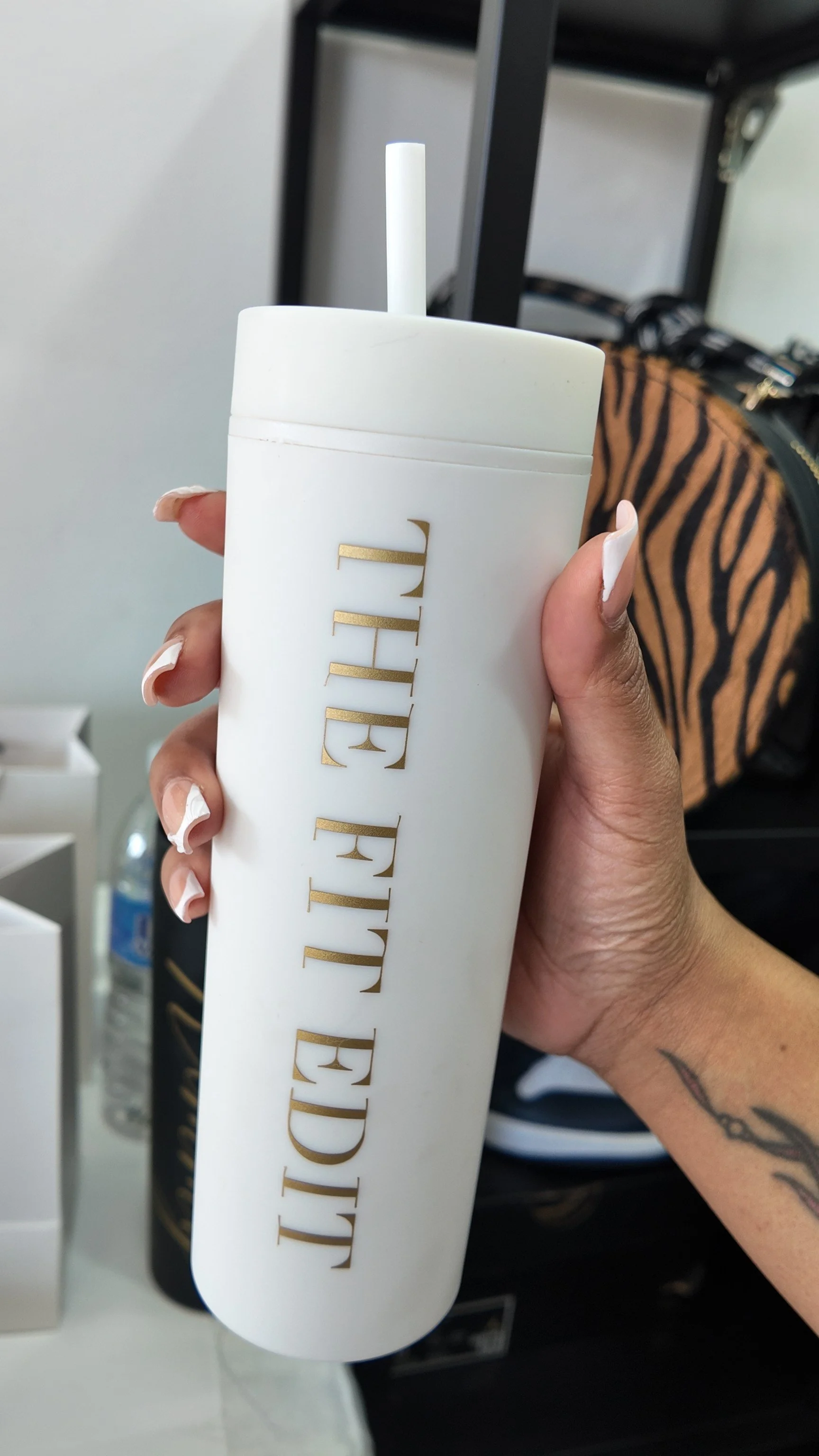 Person holding a white tumbler with gold lettering that says 'PRETTYLITTLETHING'.