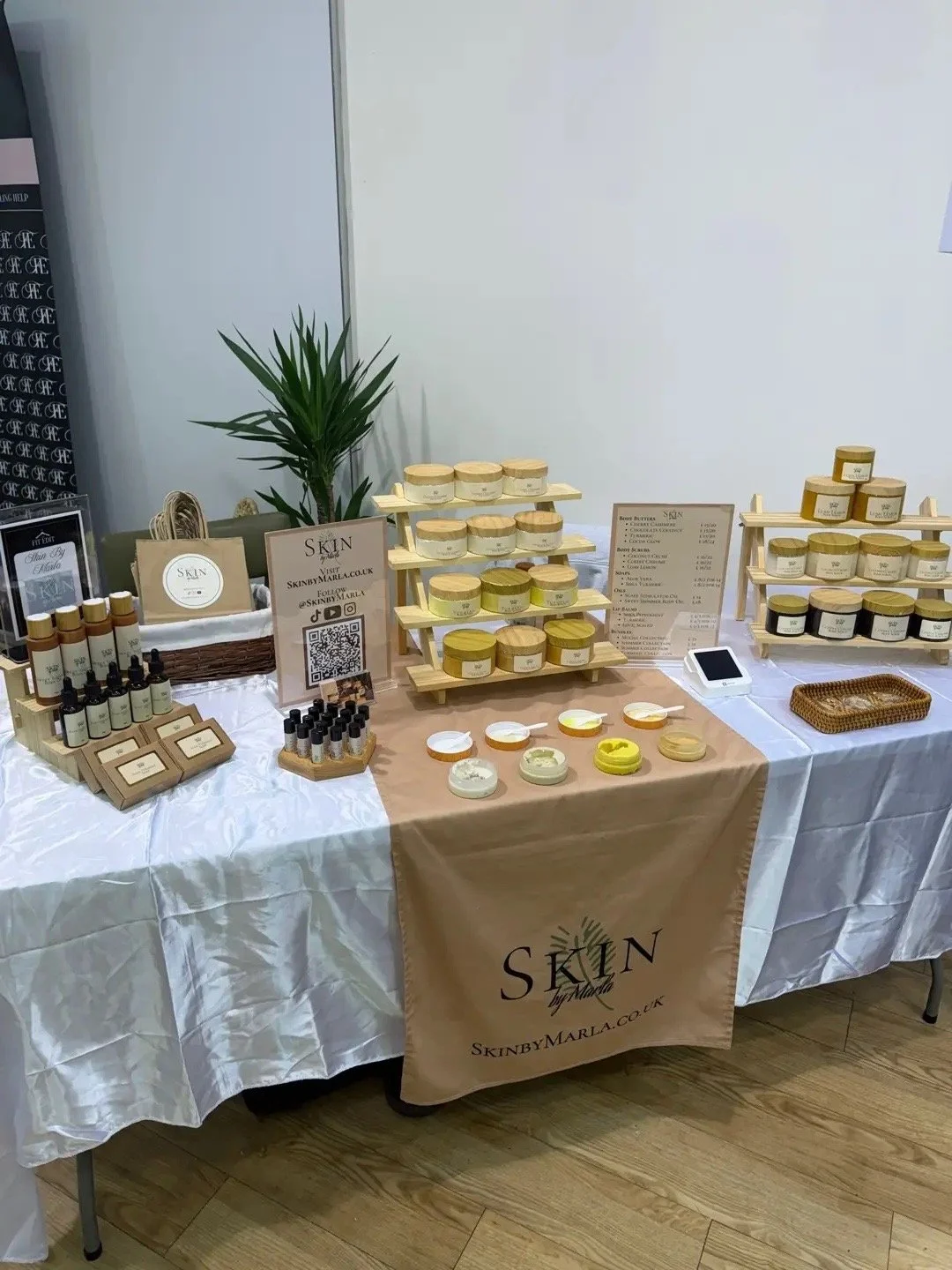 Display table with skincare products, including jars, bottles, and scent samples, set up with banners and signage for a Skin by Marla brand at an indoor event.