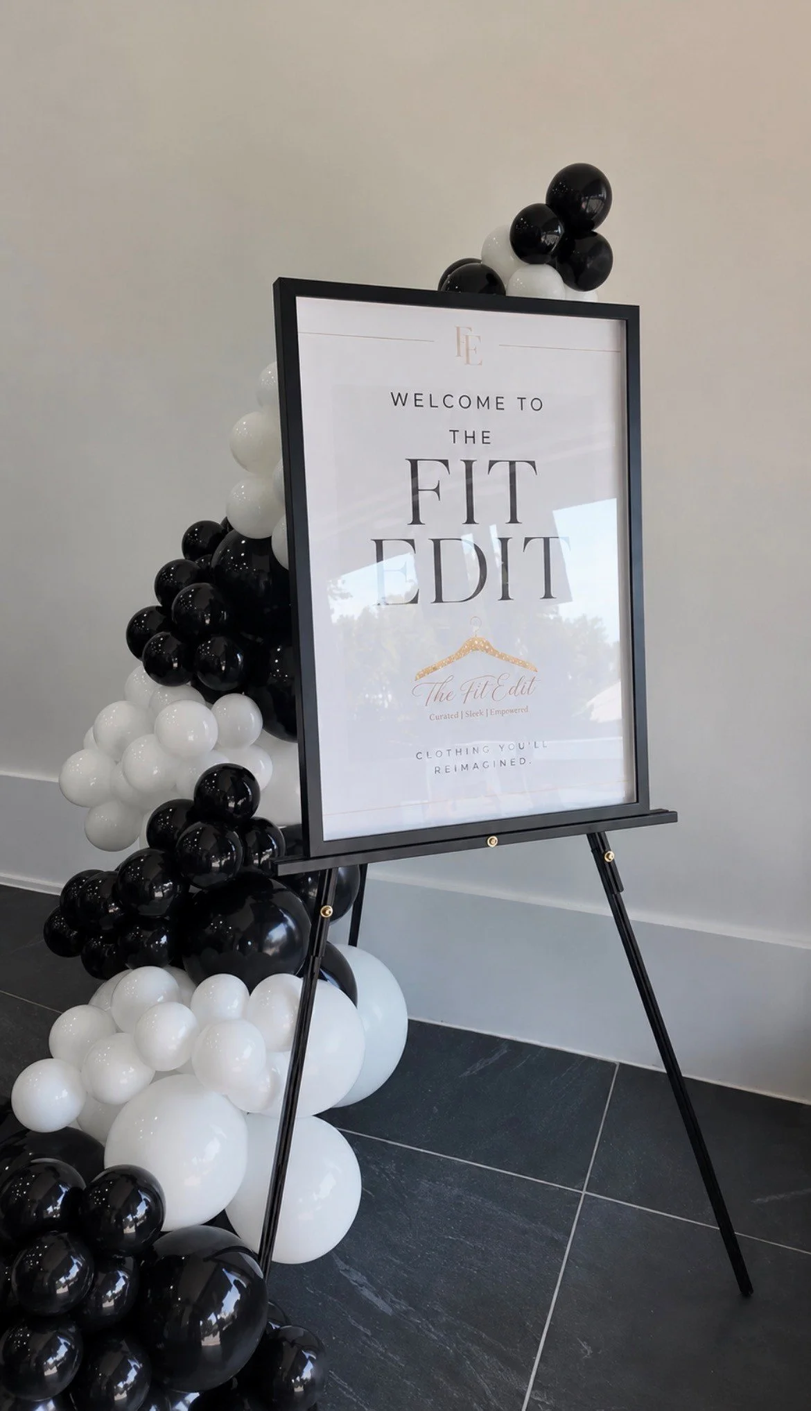 Signboard with black and white balloons surrounding it at an entrance, welcoming visitors to The Fit Edit gym or fitness studio.