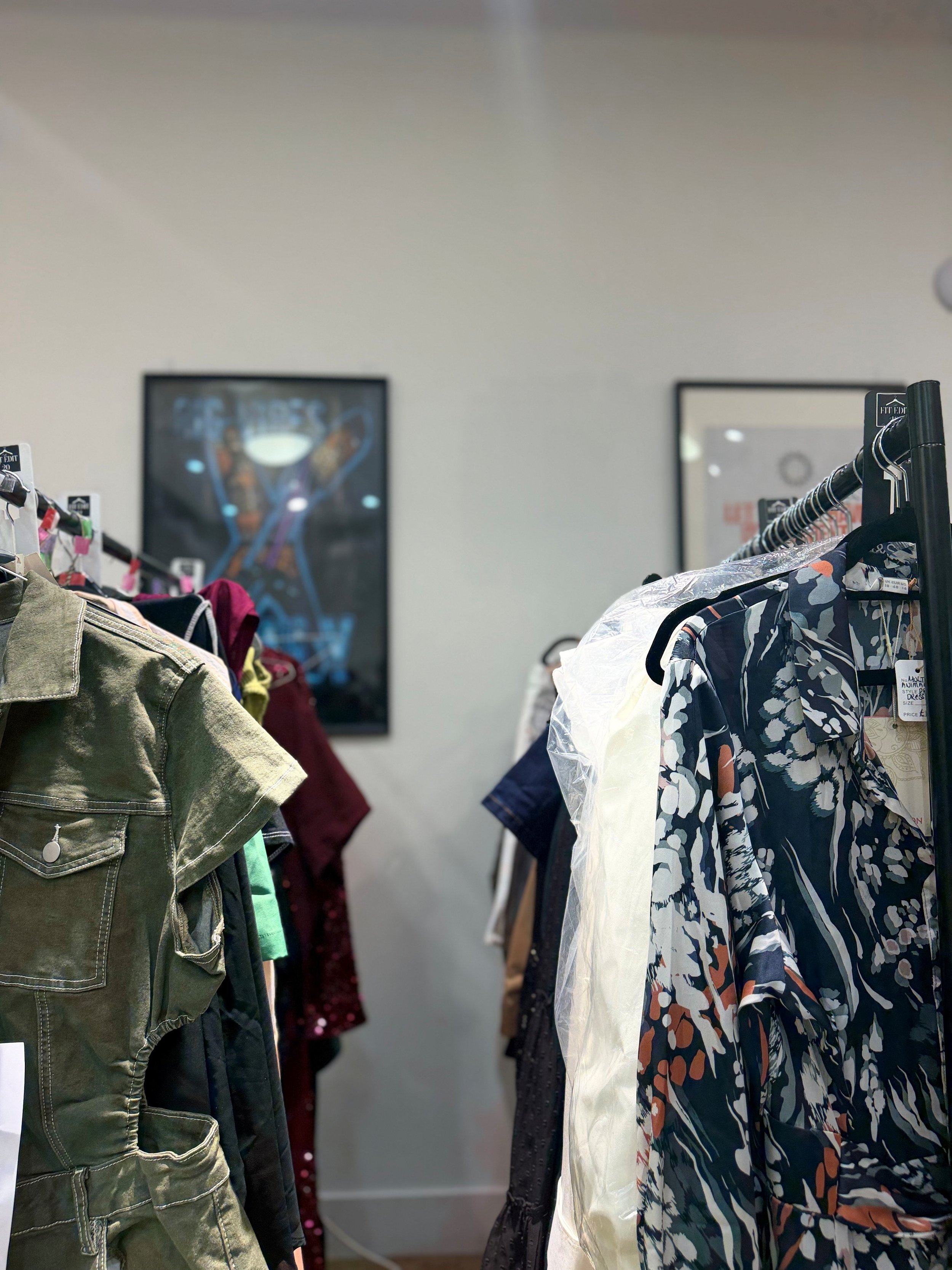 Clothing racks with various pieces of clothing including a green jacket, patterned shirts, and other garments, in a retail store.