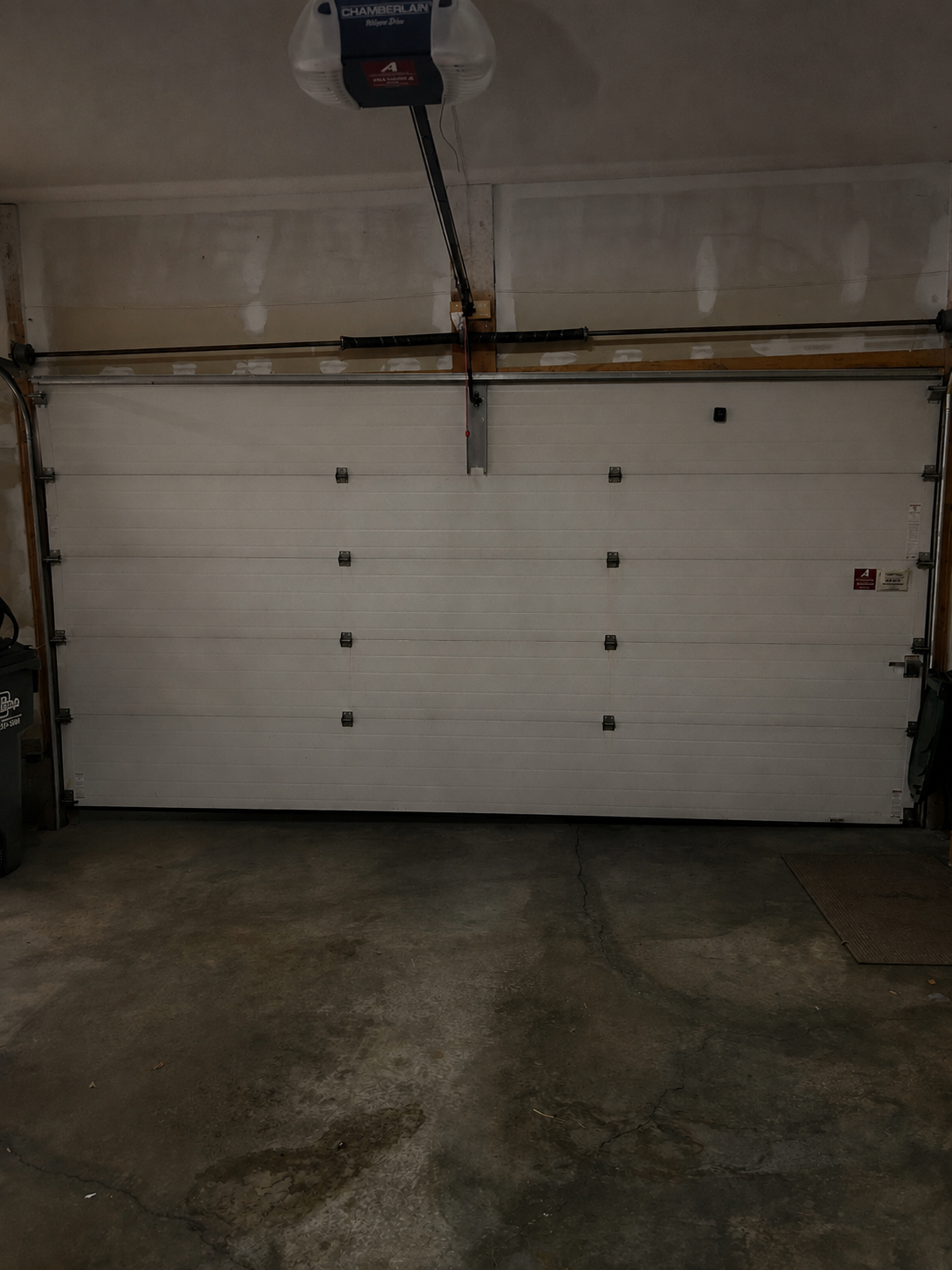 A closed white garage door with an automatic garage door opener attached to the ceiling.