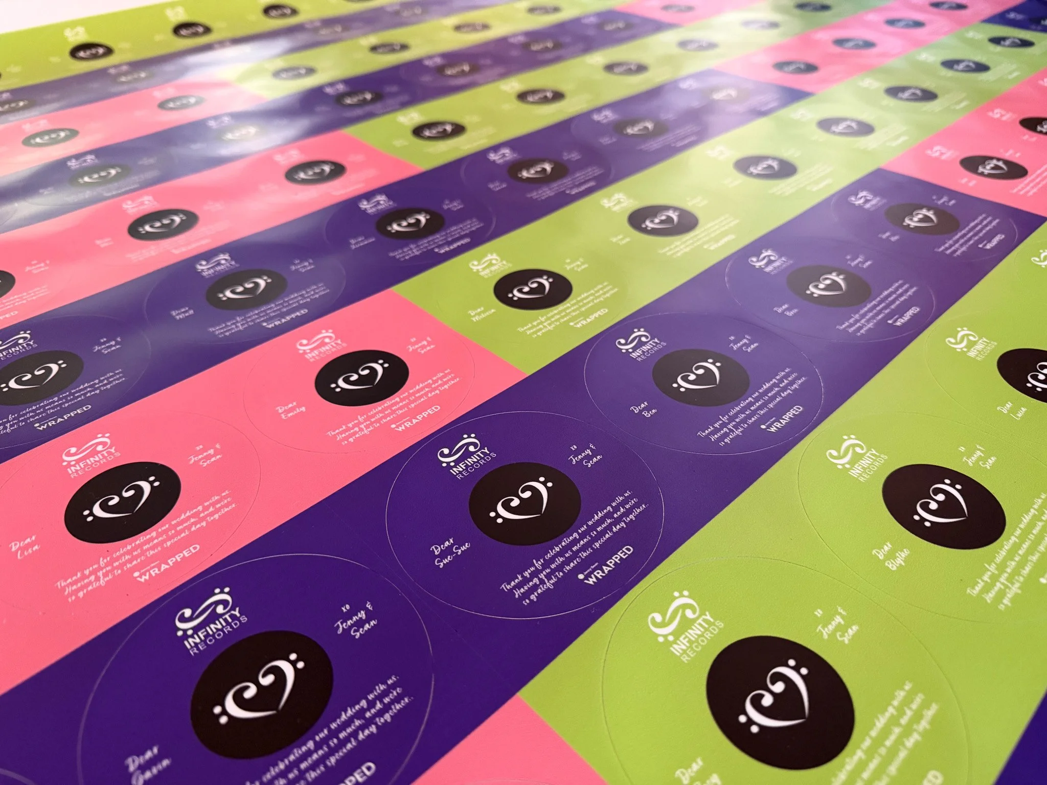 Colored stickers in pink, purple, and green with black circles and white logos for Infinity Records, arranged in rows across a surface.