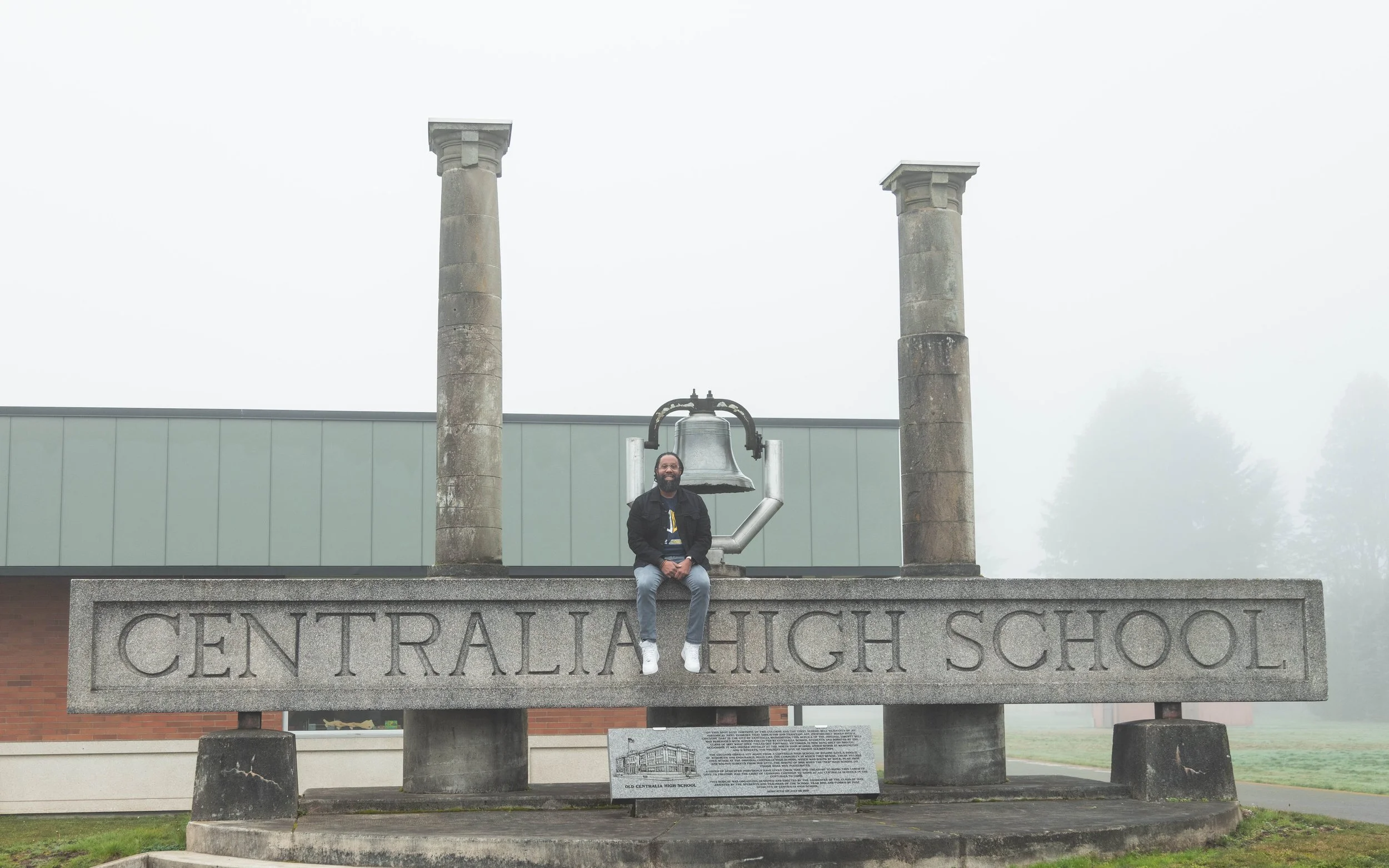Man sitting on a stone monument at Centralia High School with an overcast, foggy background.