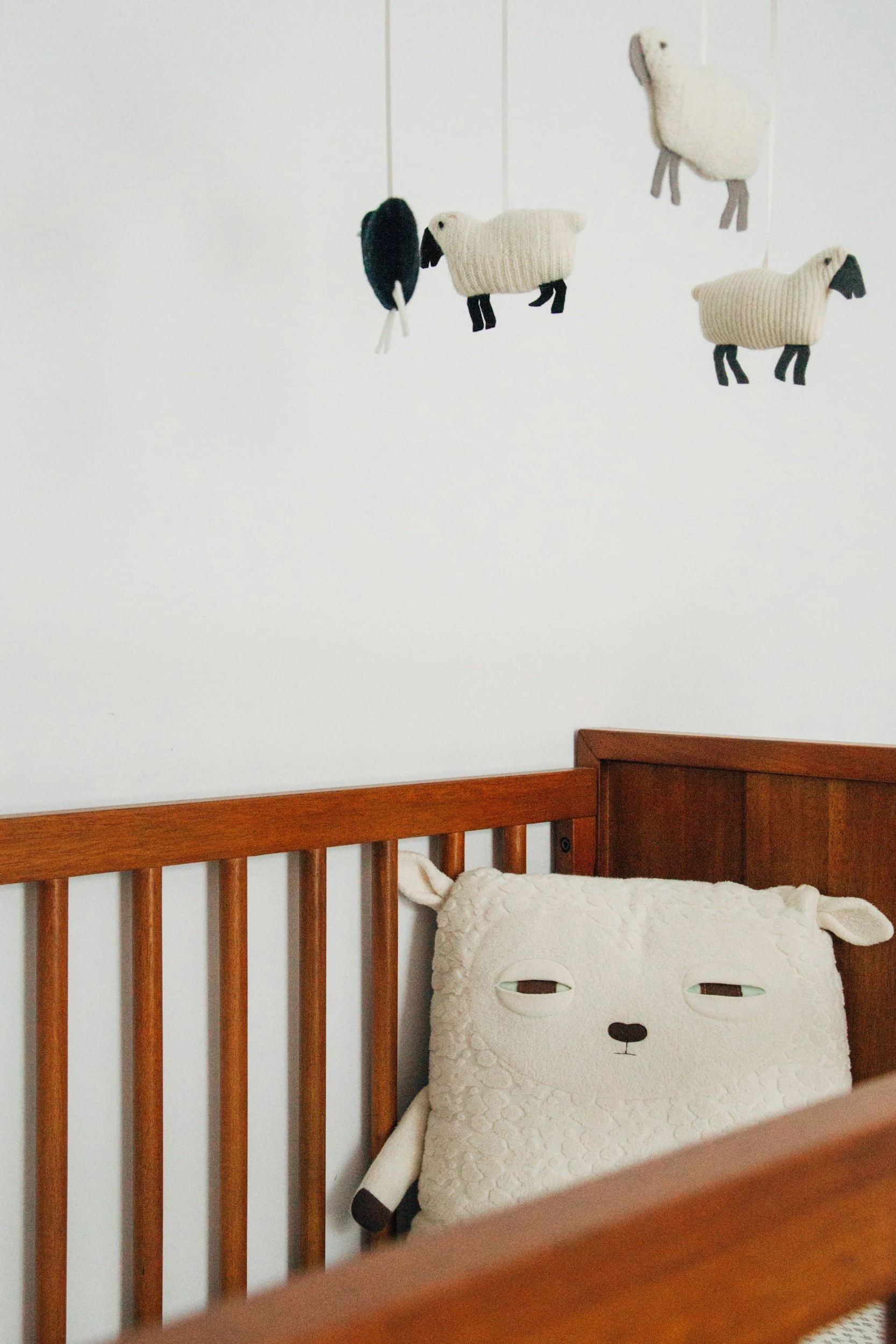 Interior of a crib with a brown wooden frame containing a plush dog-shaped pillow and three hanging fabric animal dolls on a wall. For safe sleep, all items must be removed from the crib prior to placing baby on their back to sleep.