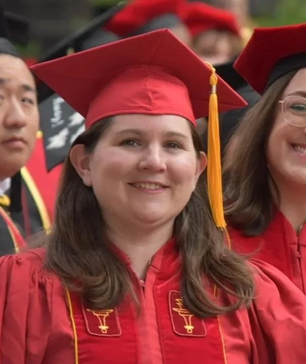 A woman in red graduation gown and cap smiling at a graduation ceremony.
