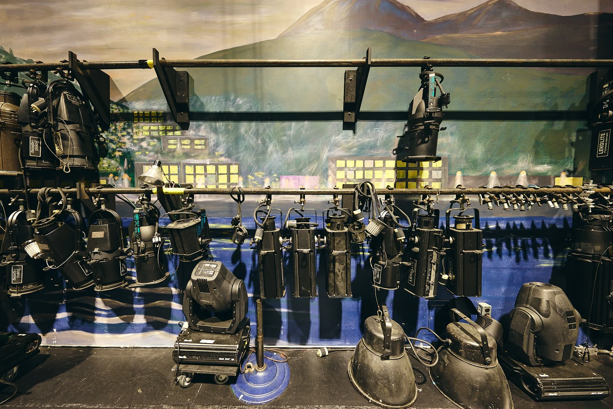 Display of stage lighting equipment and lenses in front of a mountain landscape mural.
