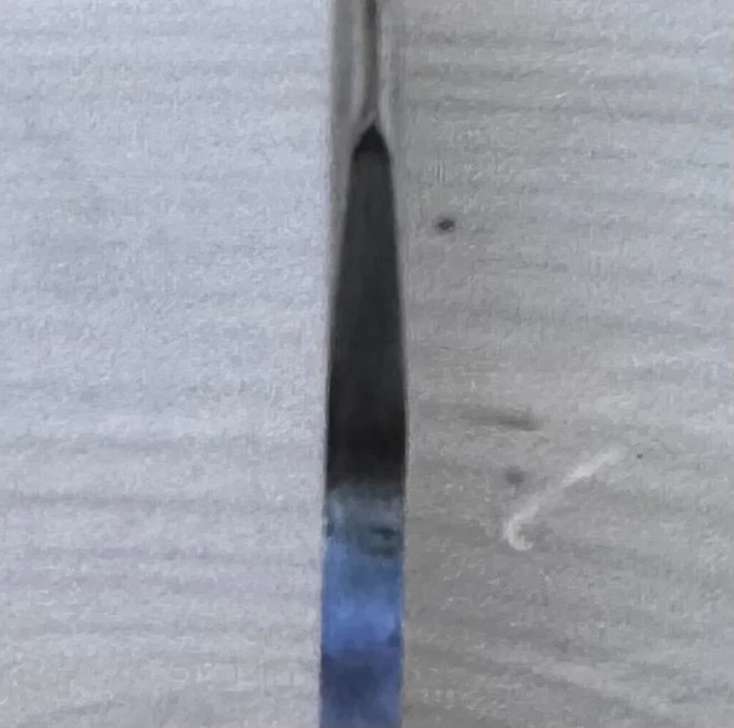 A close-up of a wood surface with a narrow, elongated gap revealing shiny blue material underneath.