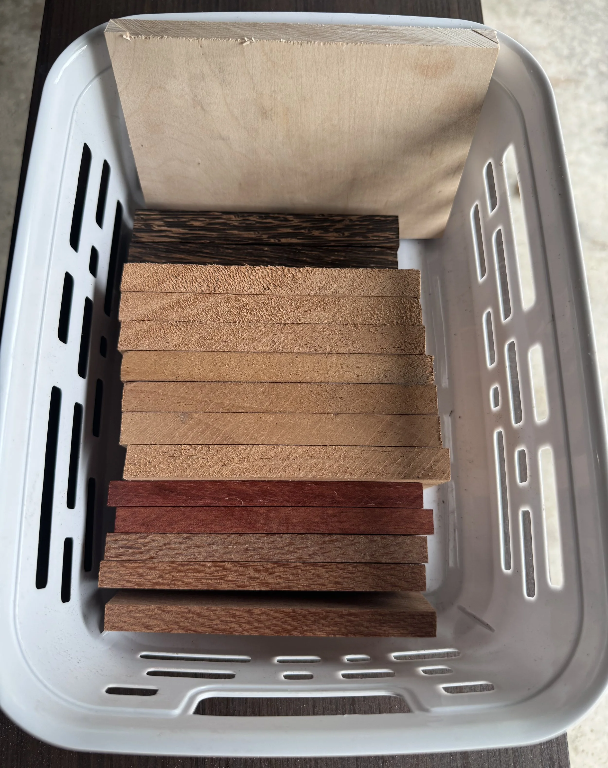 A plastic basket containing various wooden paint stir sticks, arranged vertically and showing different wood grains and finishes.