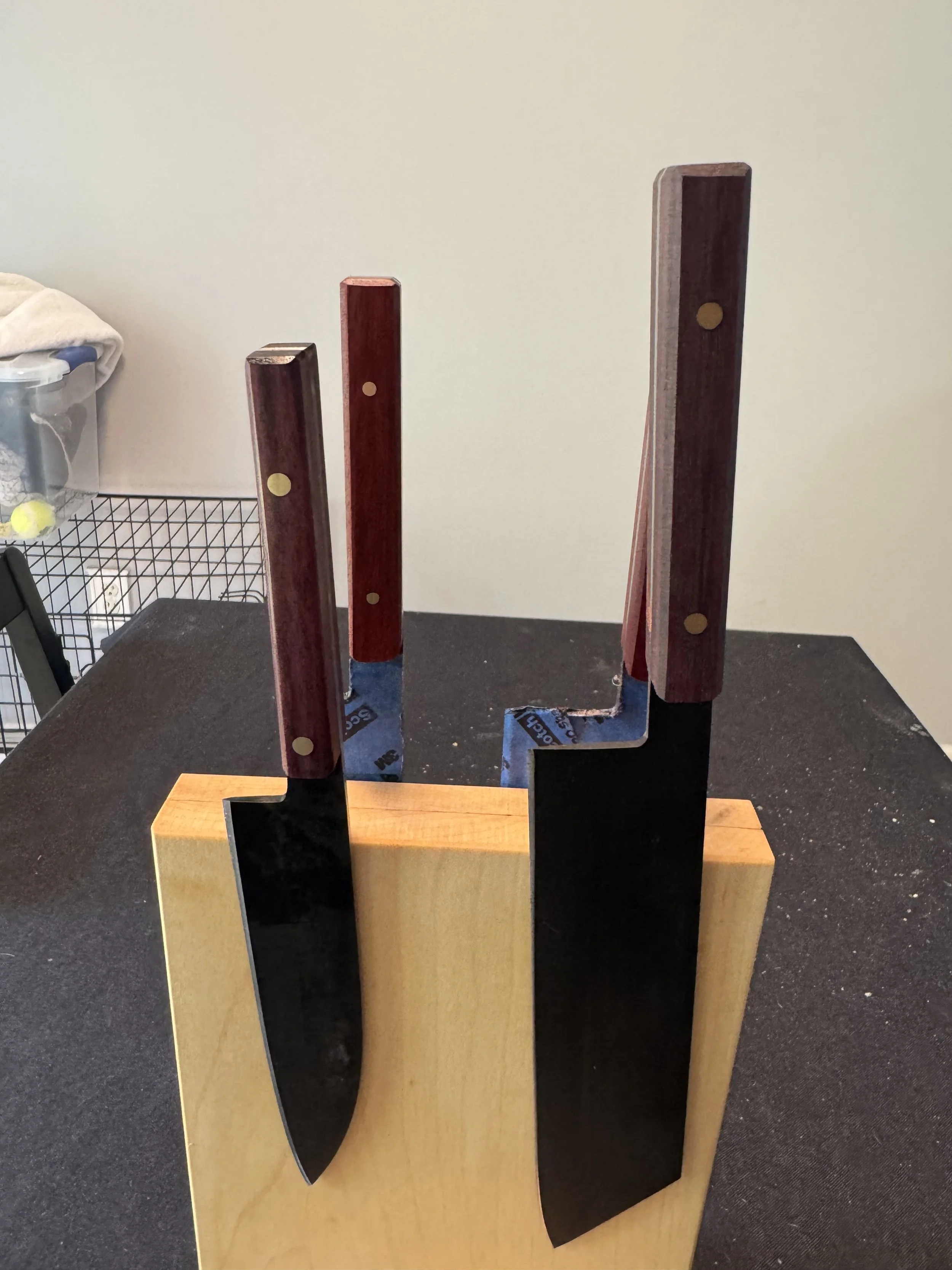 A trophy with a wooden base and four vertical wooden slabs attached to a metal frame, with one slab painted black and the others in reddish wood color, standing on a wooden platform on a black surface.