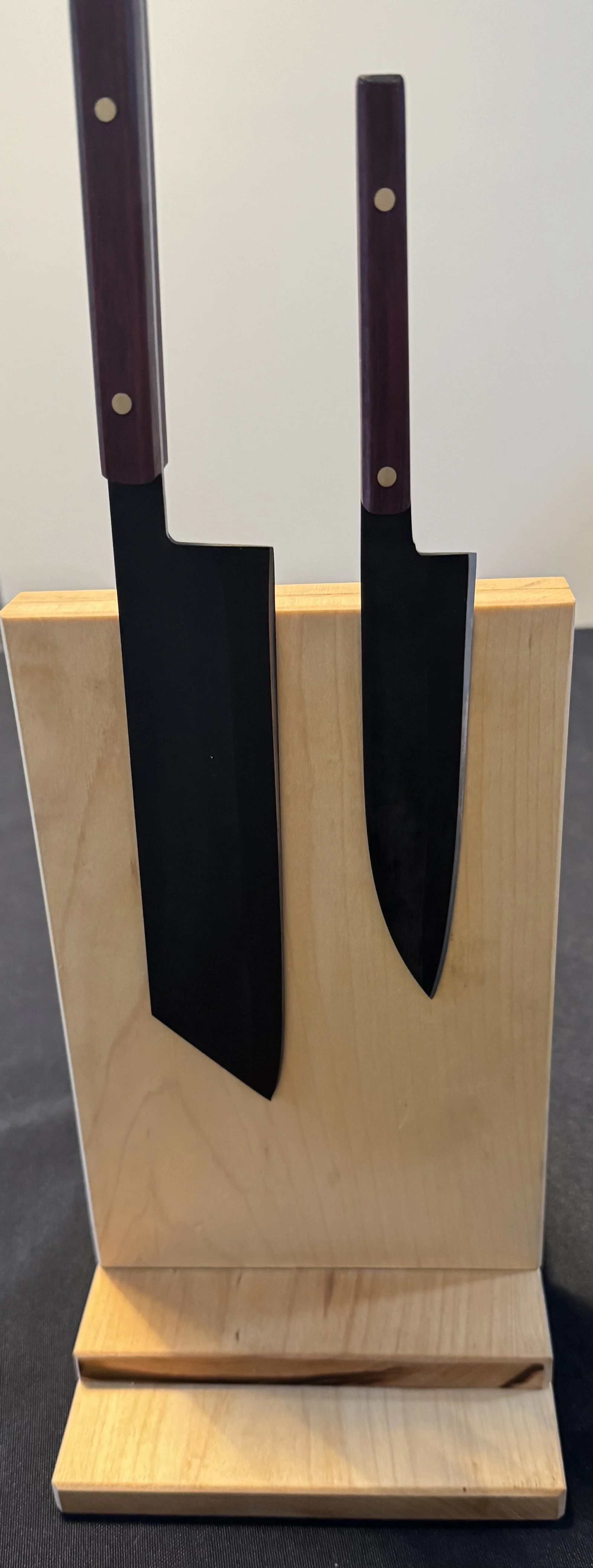 Two Japanese-style kitchen knives with wooden handles are mounted upright on a wooden display stand.