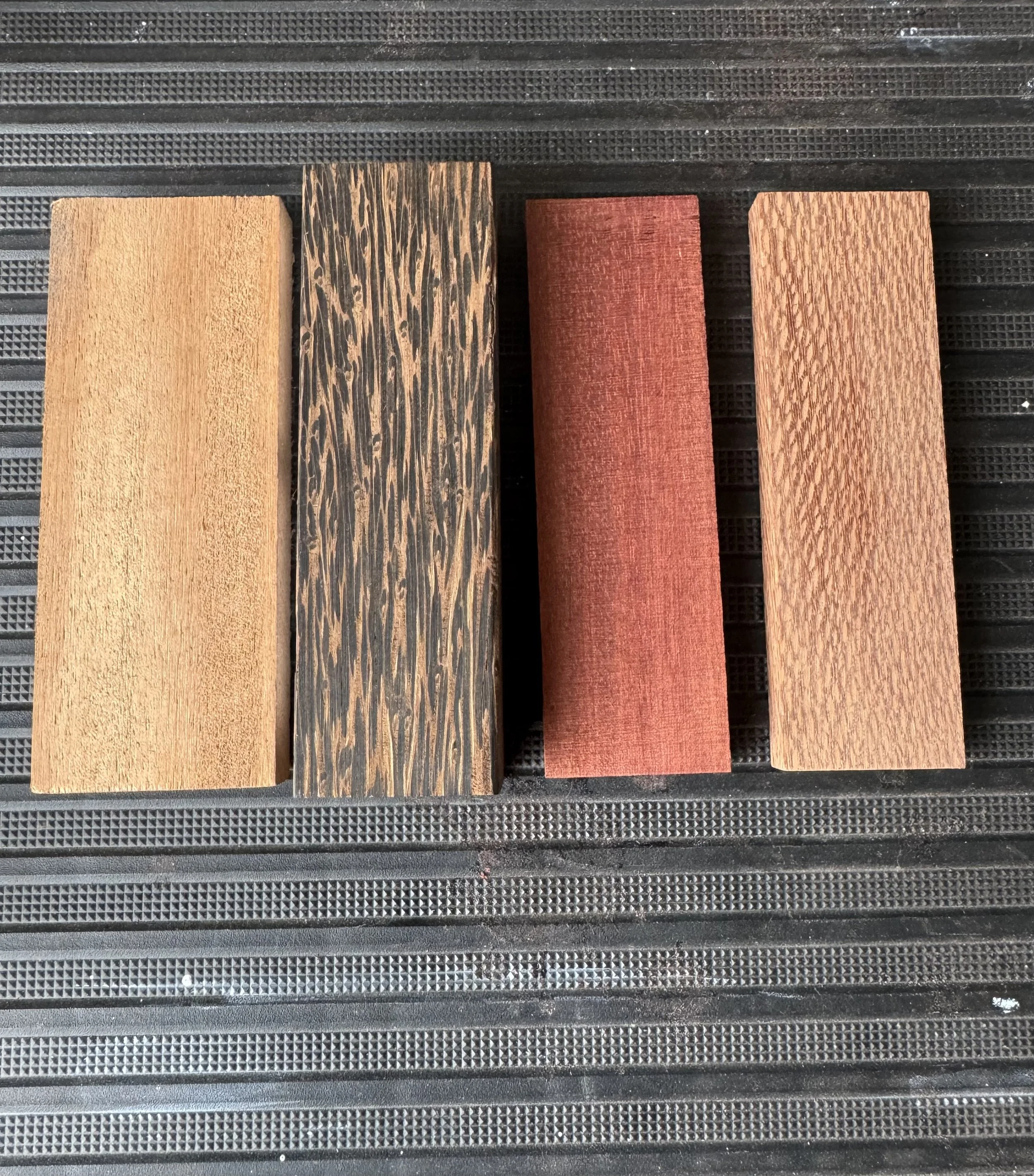 Four wooden samples with different finishes placed on a black textured surface.