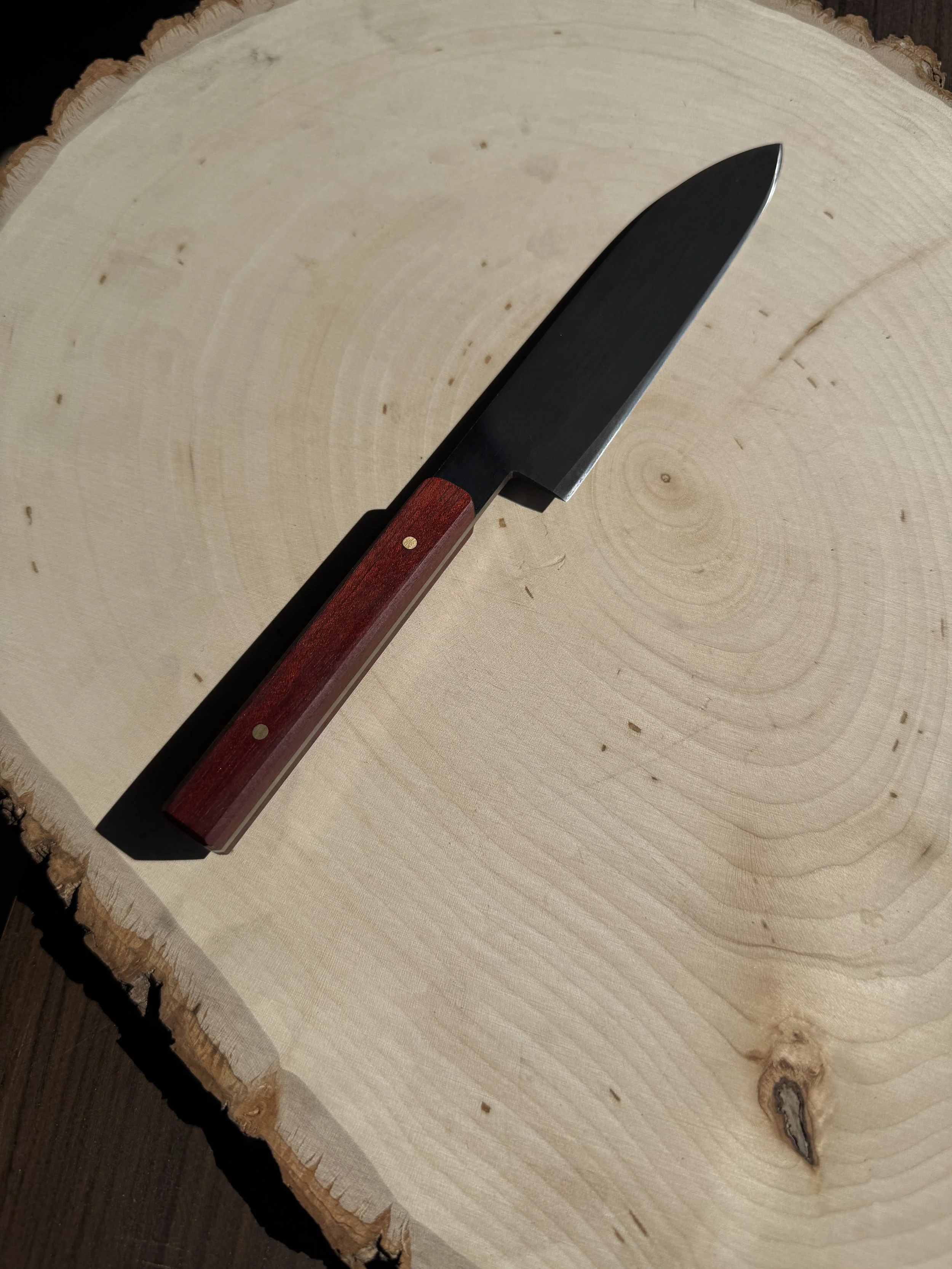 A small kitchen knife with a black blade and wooden handle rests on a cross-section of a tree trunk.