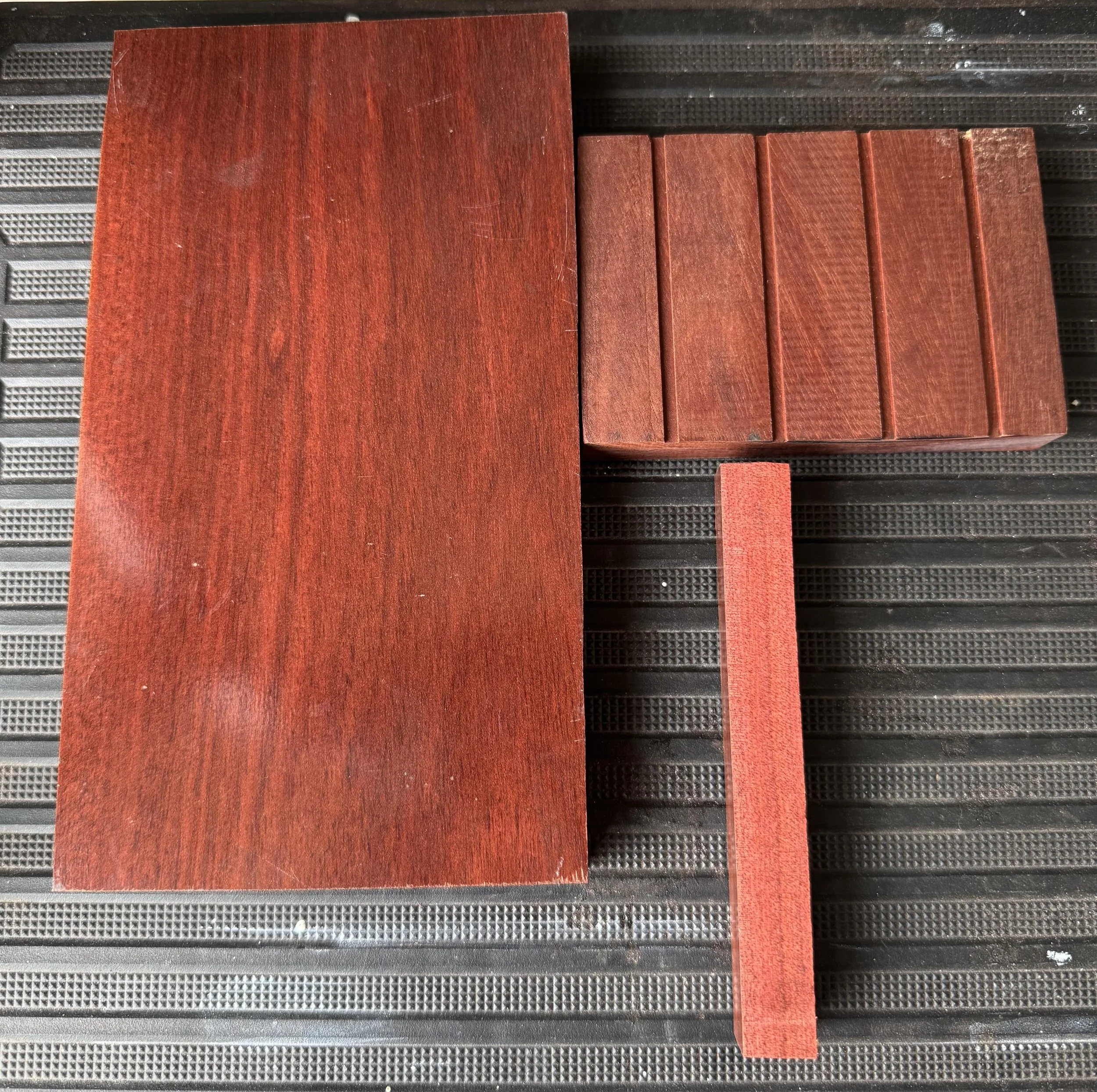Close-up of several small red wooden slats and one larger wooden piece on a black textured surface.