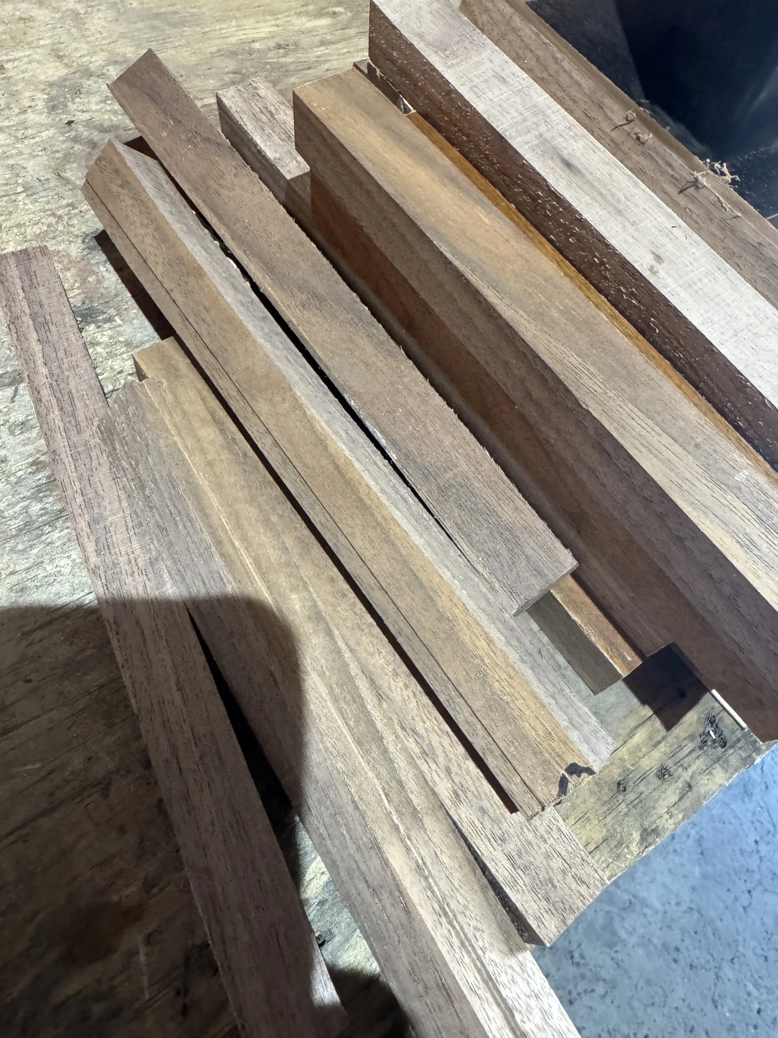 Close-up of stacked aged wooden planks or beams, arranged on a concrete floor.