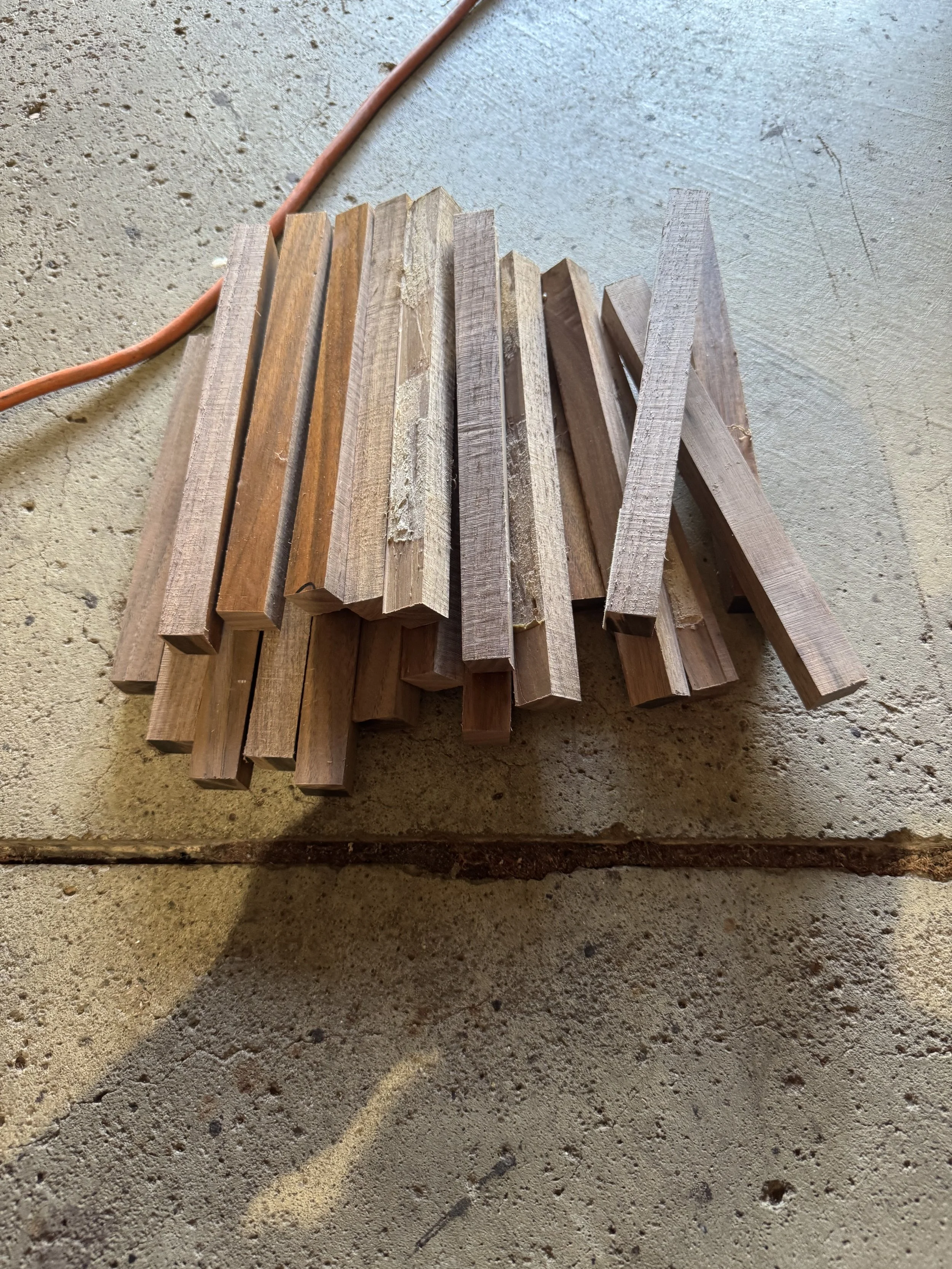 Several wooden sticks stacked on a concrete floor with an orange electrical cord near them.