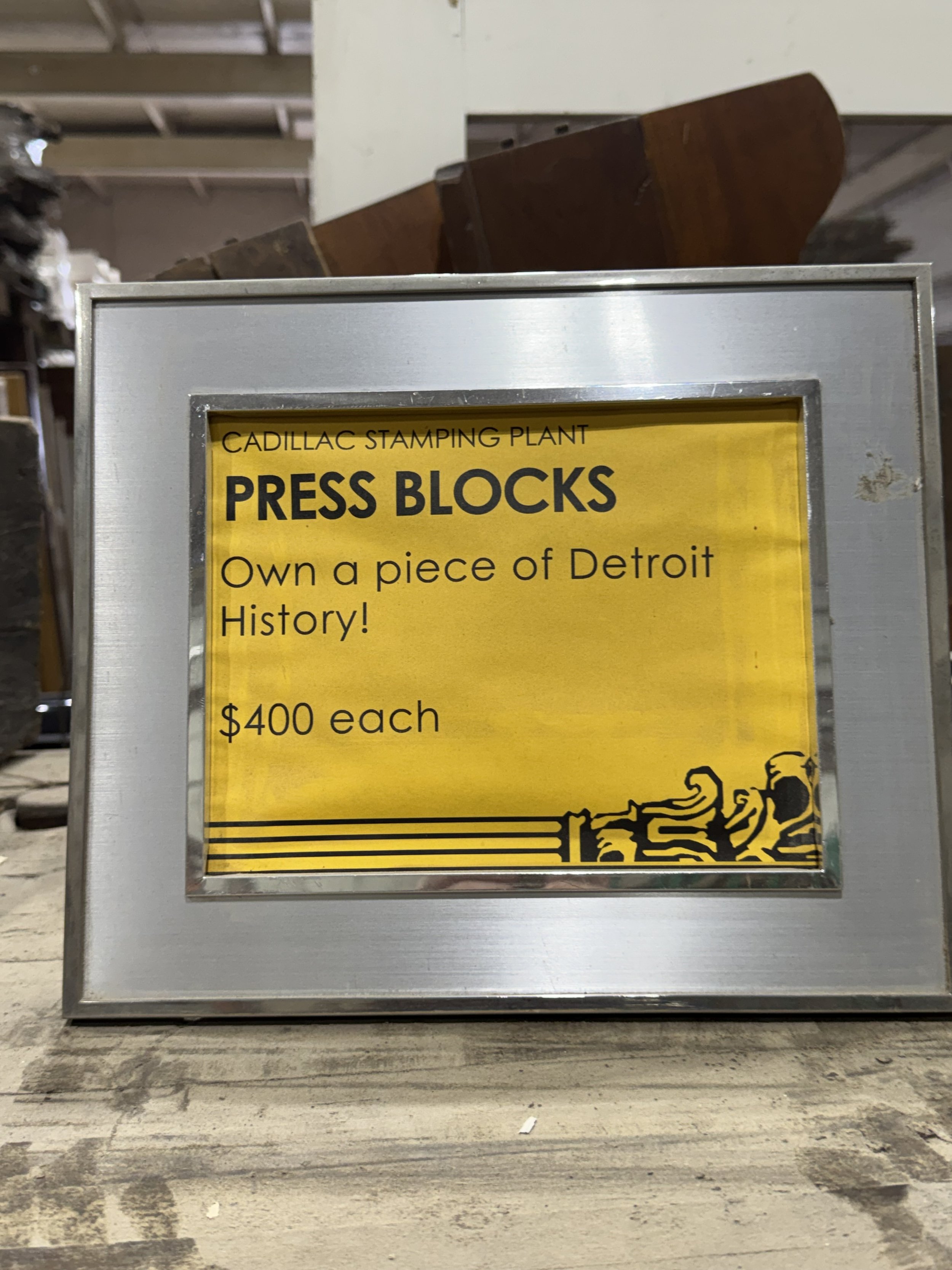 Sign with yellow background, black text, and a graphic of a tiger; advertising press blocks for sale at Cadillac Stamping Plant for $400 each.