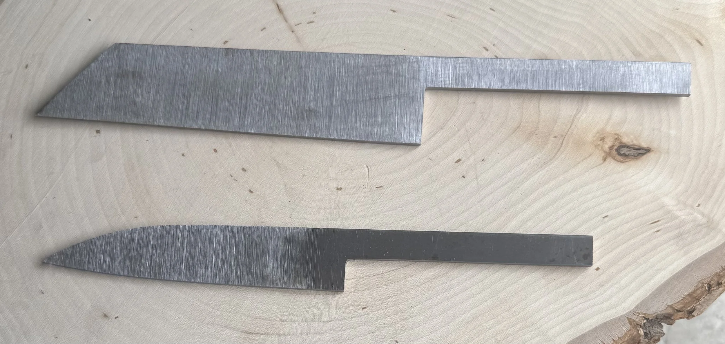 Two metal scrapers with flat blades and pointed ends placed on a light-colored wooden surface.