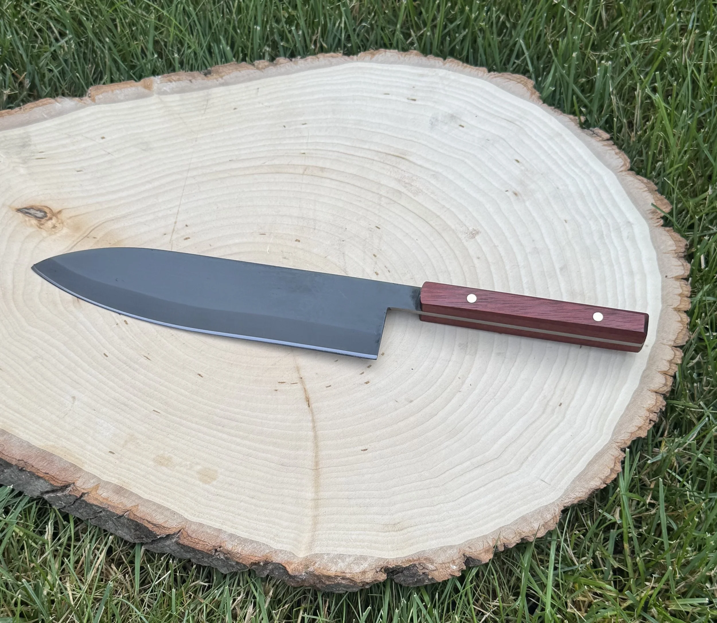 A large cut tree trunk with visible growth rings placed on grass with a knife resting on it.