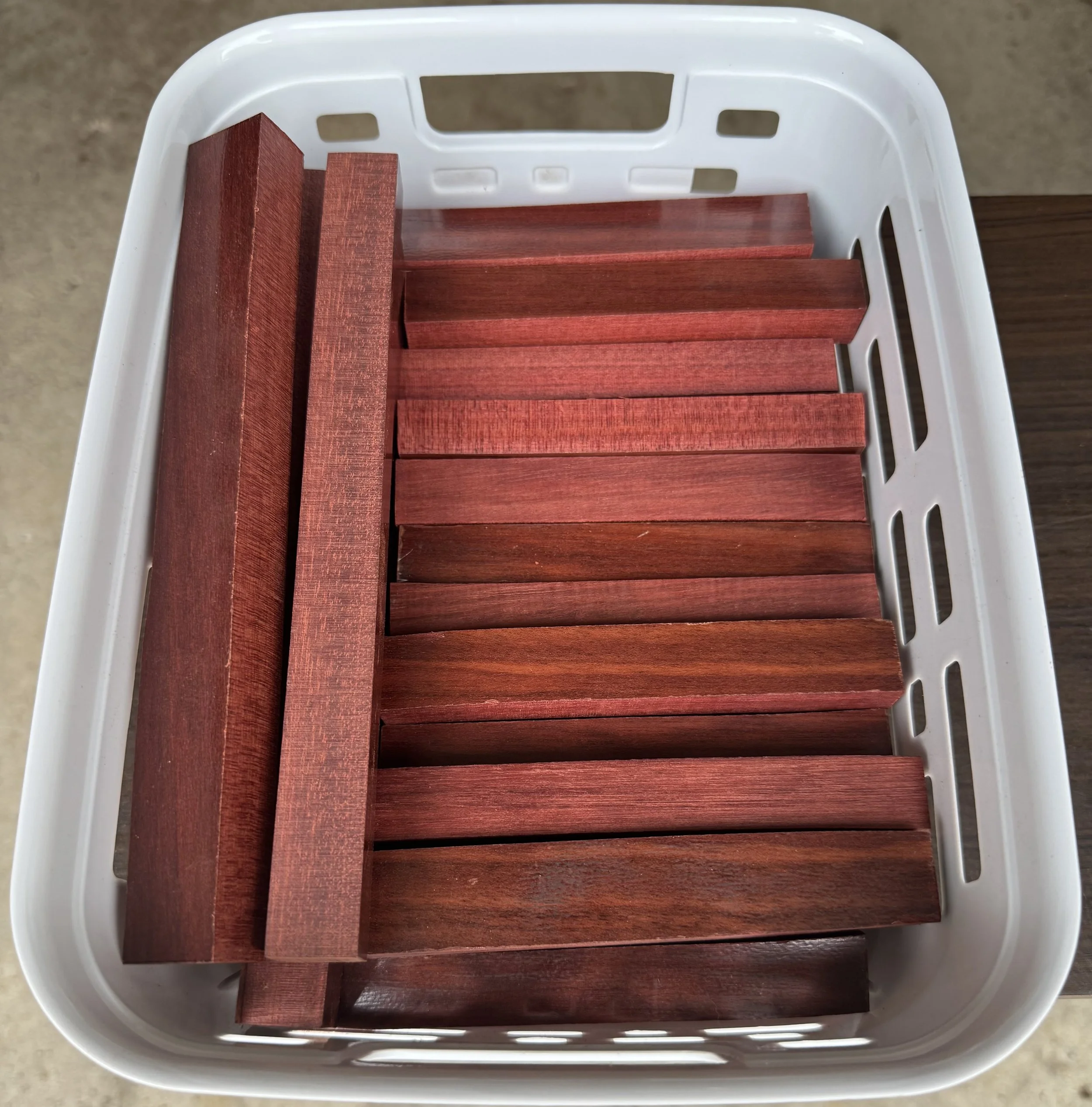 A white plastic basket containing several reddish-brown wooden bars or pieces, with a textured surface and varying lengths, placed on a flat surface.