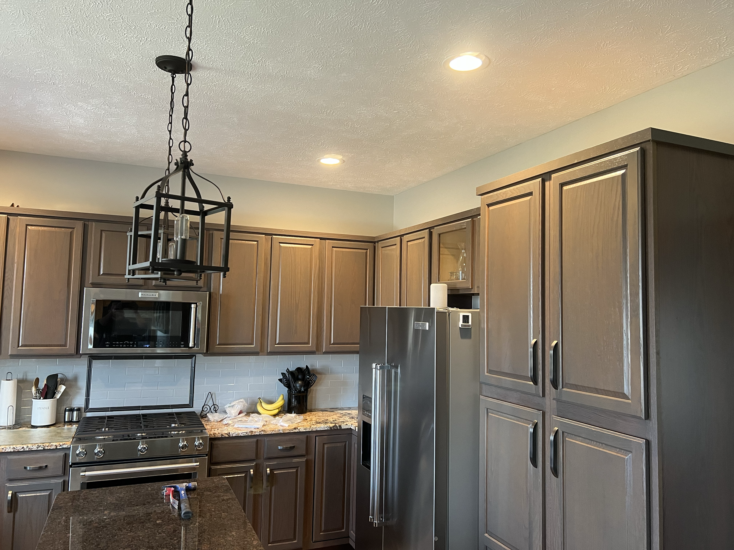 Kitchen with wooden cabinets, stainless steel appliances, a gas stove, black utensils, a bunch of bananas, and a black hanging light fixture.